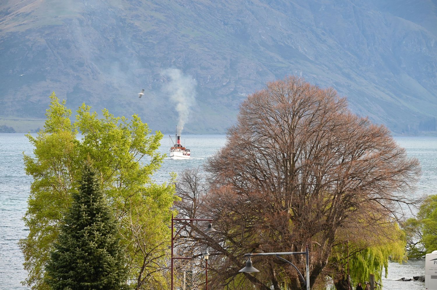 A steamboat glides across a mountain lake framed by autumn trees with misty peaks in the background.