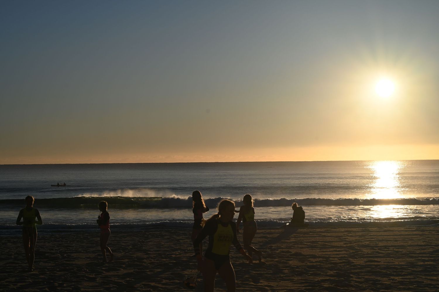 Silhouettes of people playing on a sandy beach at golden sunset with ocean waves in the background.