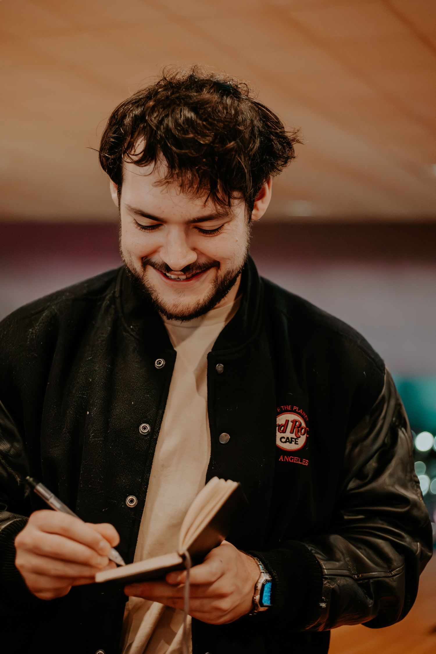 James Marriott in a black jacket smiling while writing something down at a table.