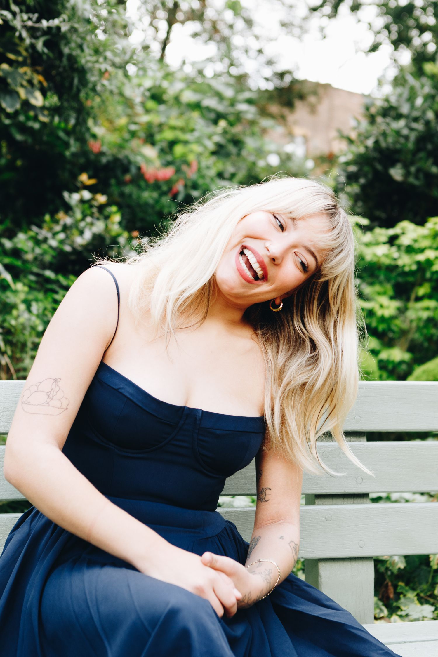 Cate Canning in navy dress laughs joyfully while sitting in garden setting.