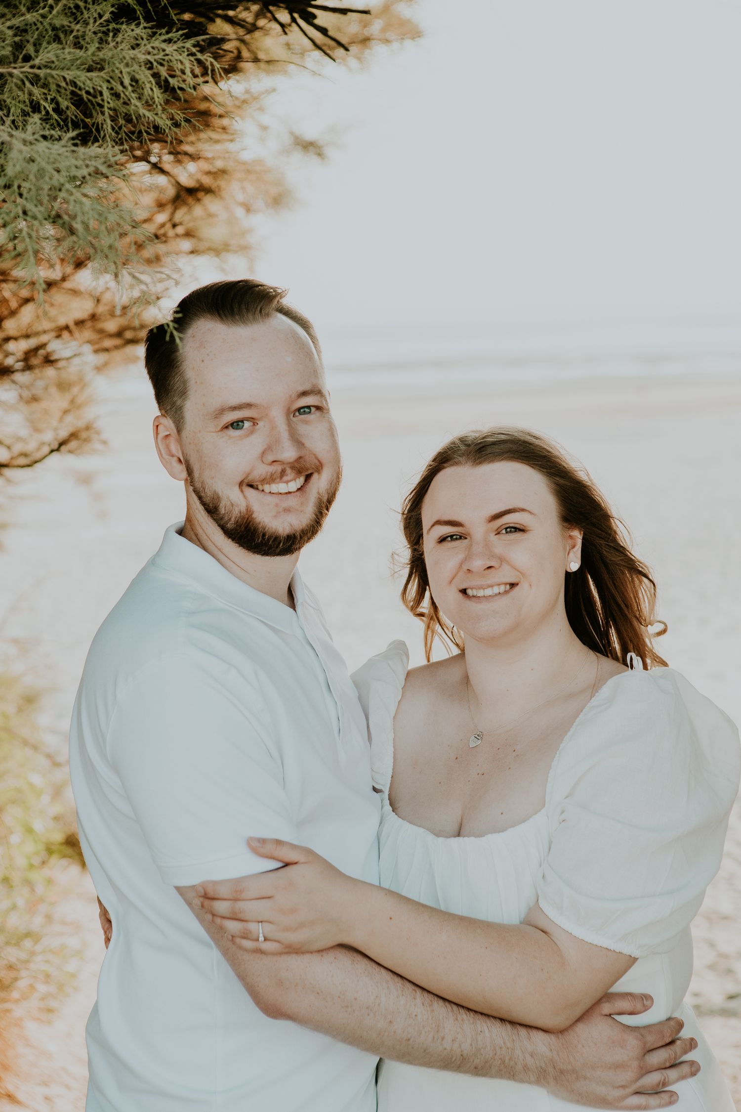 Happy couple embracing outdoors in white outfits during sunset photoshoot.