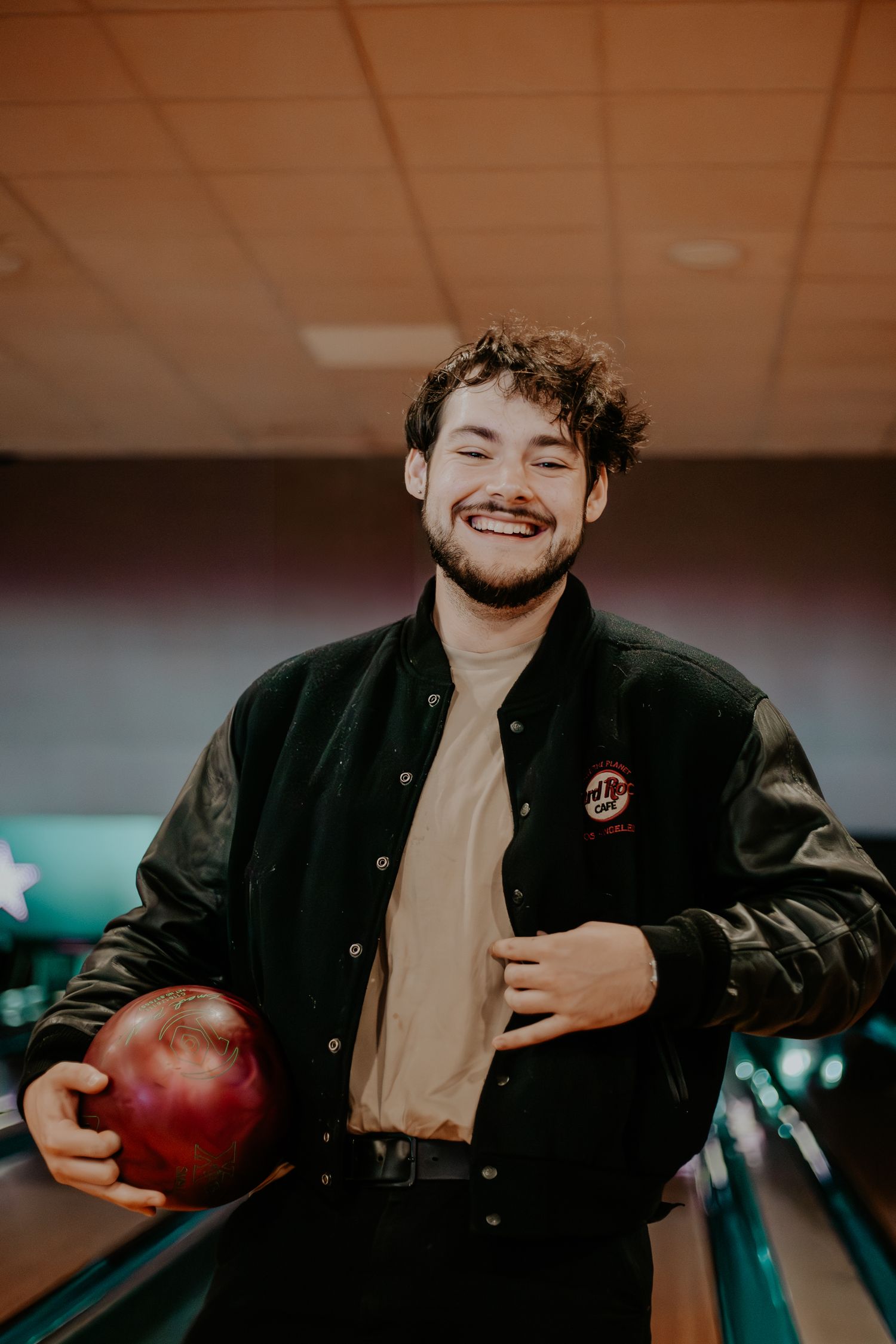 James Marriott holding a red bowling ball while smiling in a bowling alley.
