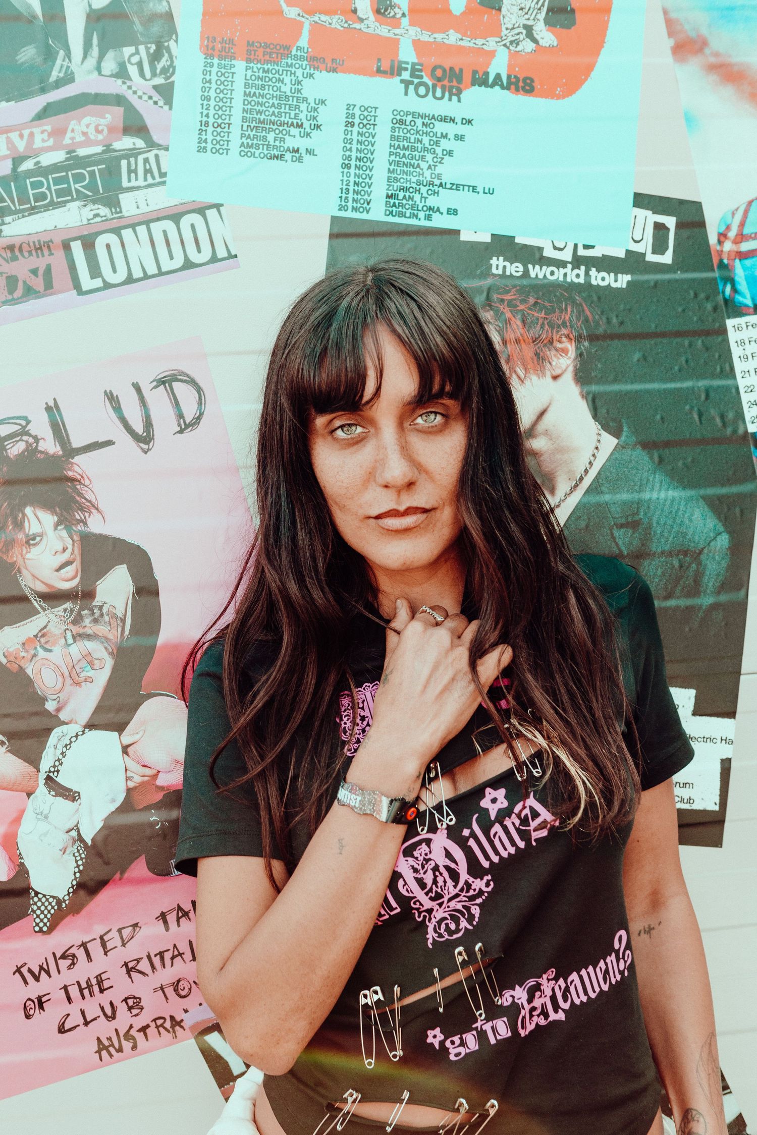 Jesse Jo Stark in a band t-shirt posing against a collage of concert posters and tour dates, from Bludfest.