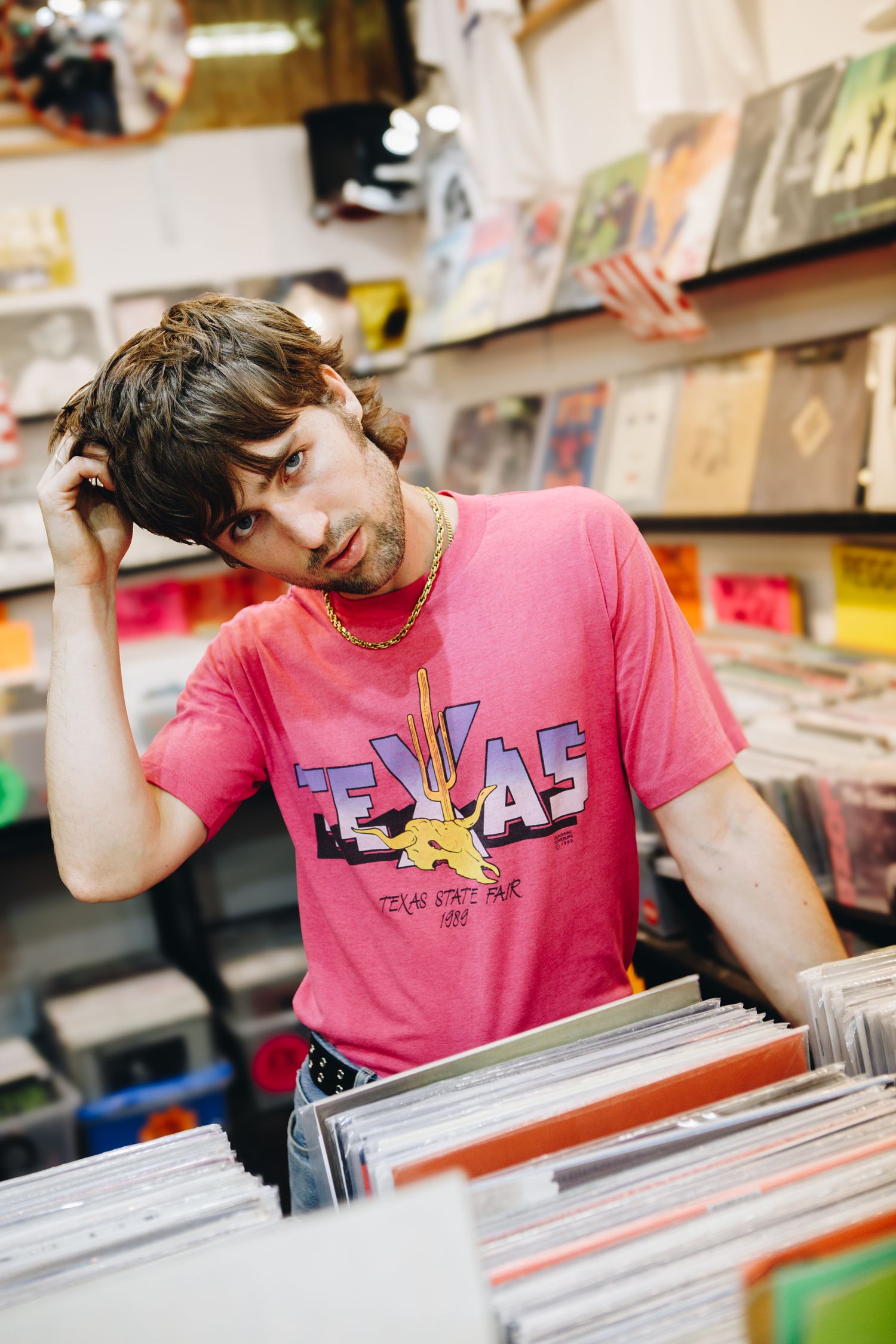 Will Joseph Cook posing in a pink Texas t-shirt browses through vinyl records in a music store.
