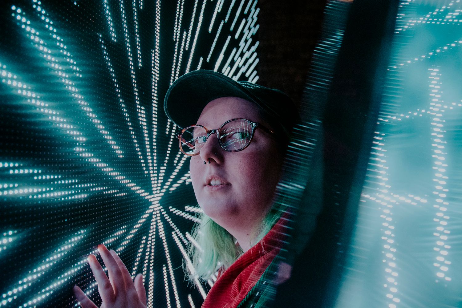 Person in cap and glasses against futuristic blue light display creating dynamic patterns.