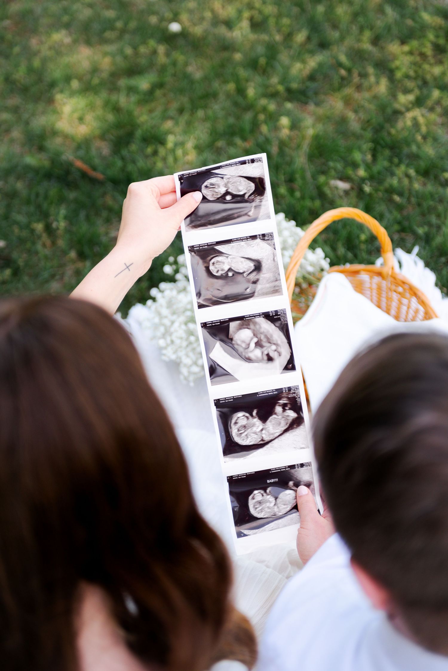 Couple looking at ultrasound strip photos together during outdoor pregnancy announcement picnic session.