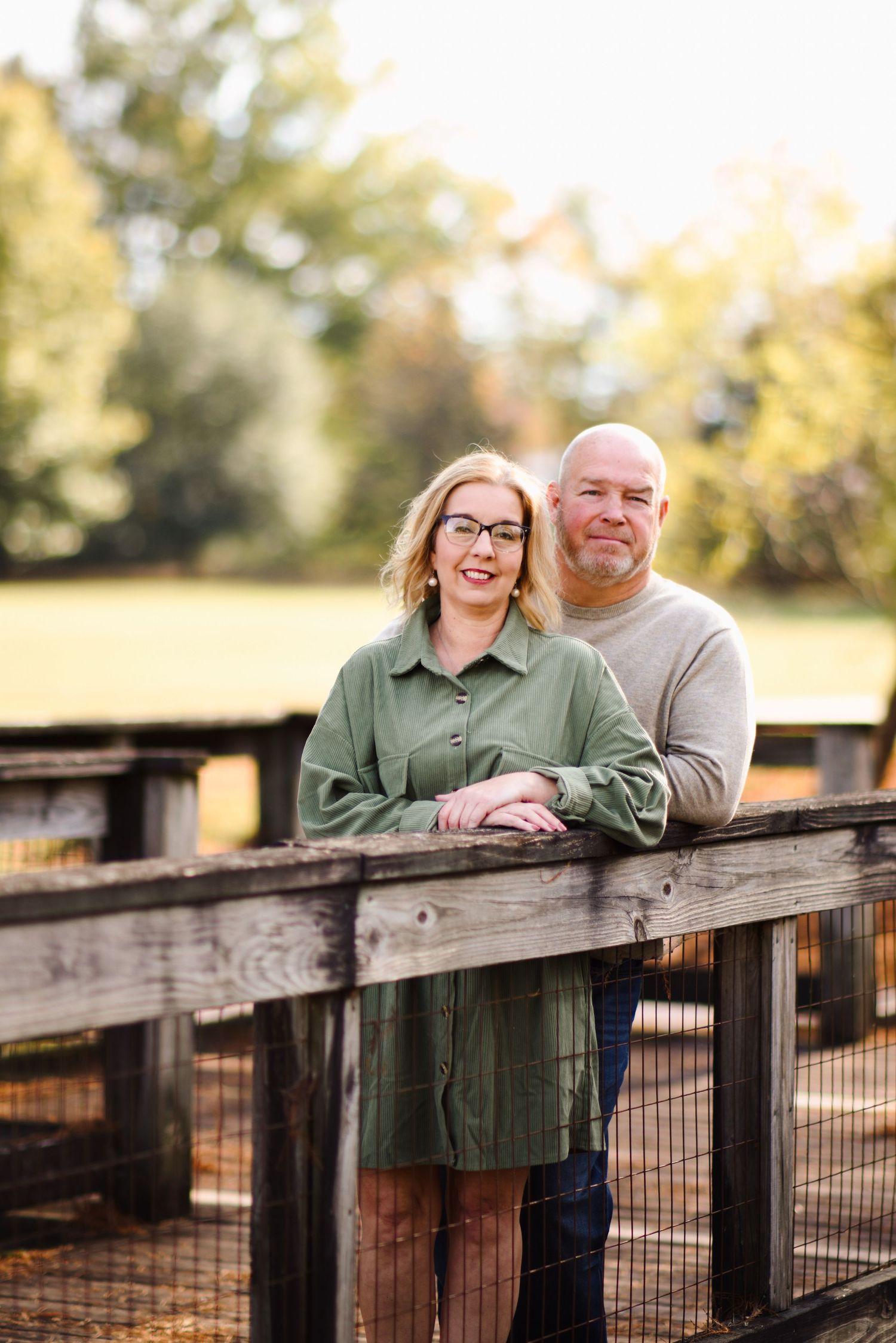 Smiling couple leans on a wooden fence outdoors in warm autumn sunlight in a park.