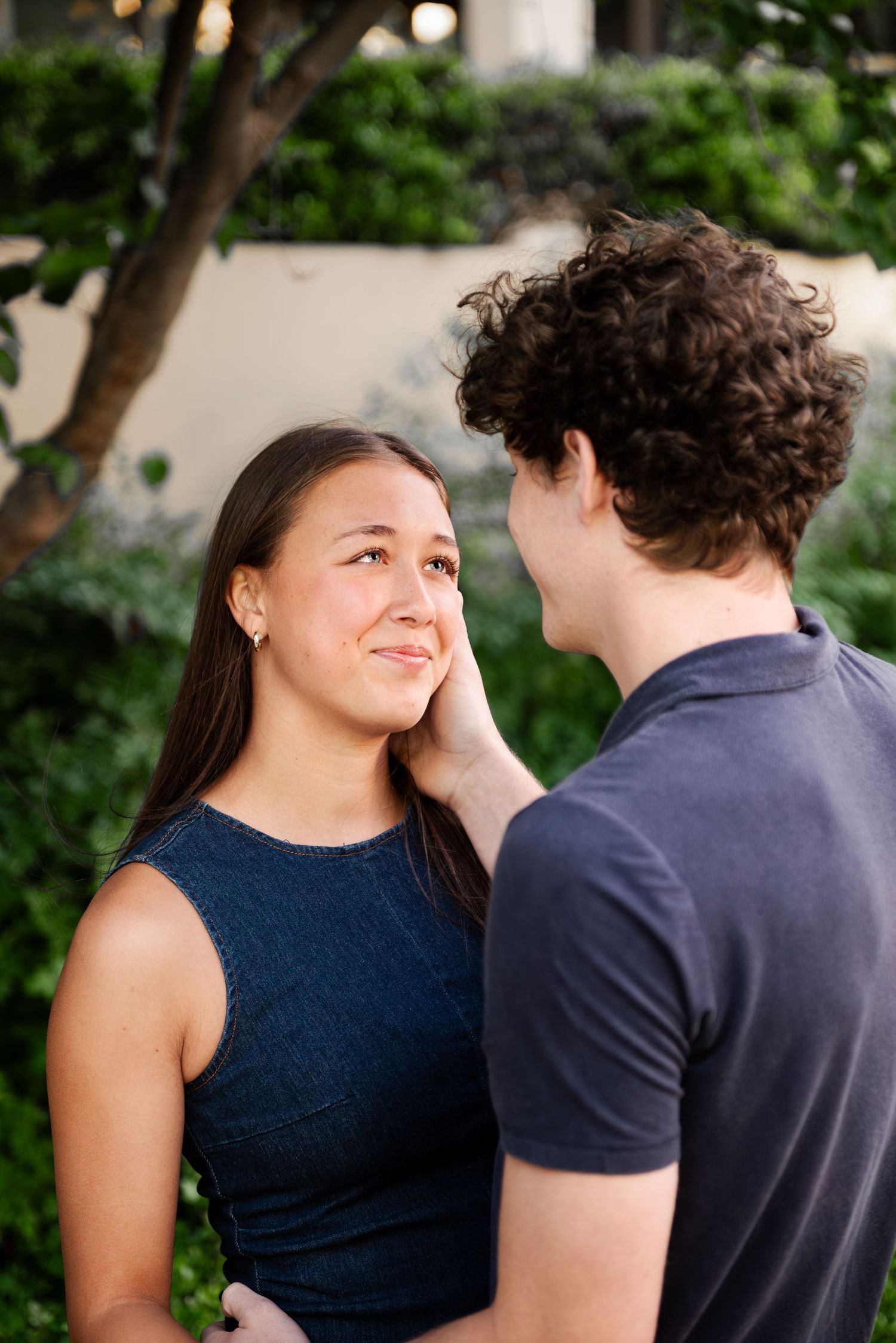 Young man tenderly touching womans face as she smiles up at him in a lush garden setting.