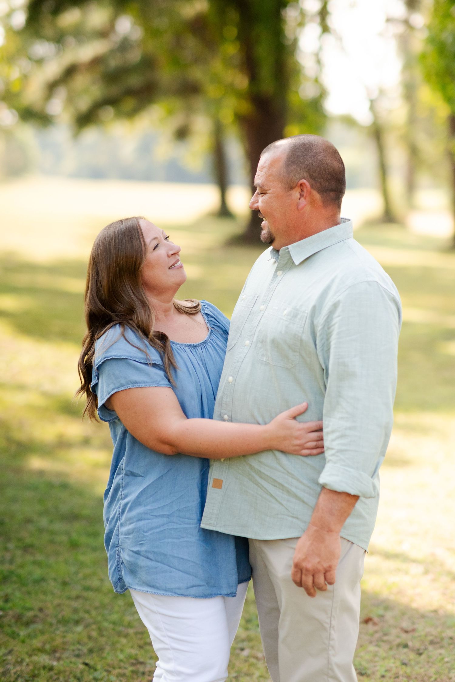 Middle-aged couple smiling and embracing each other outdoors in a sunny green park setting.