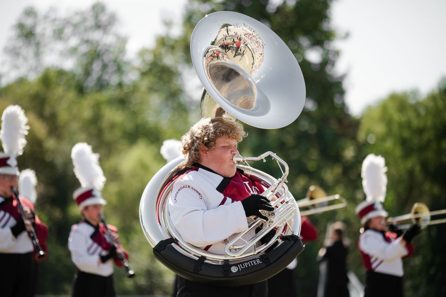 A marching band member plays a large suba tuba during an outdoor performance.