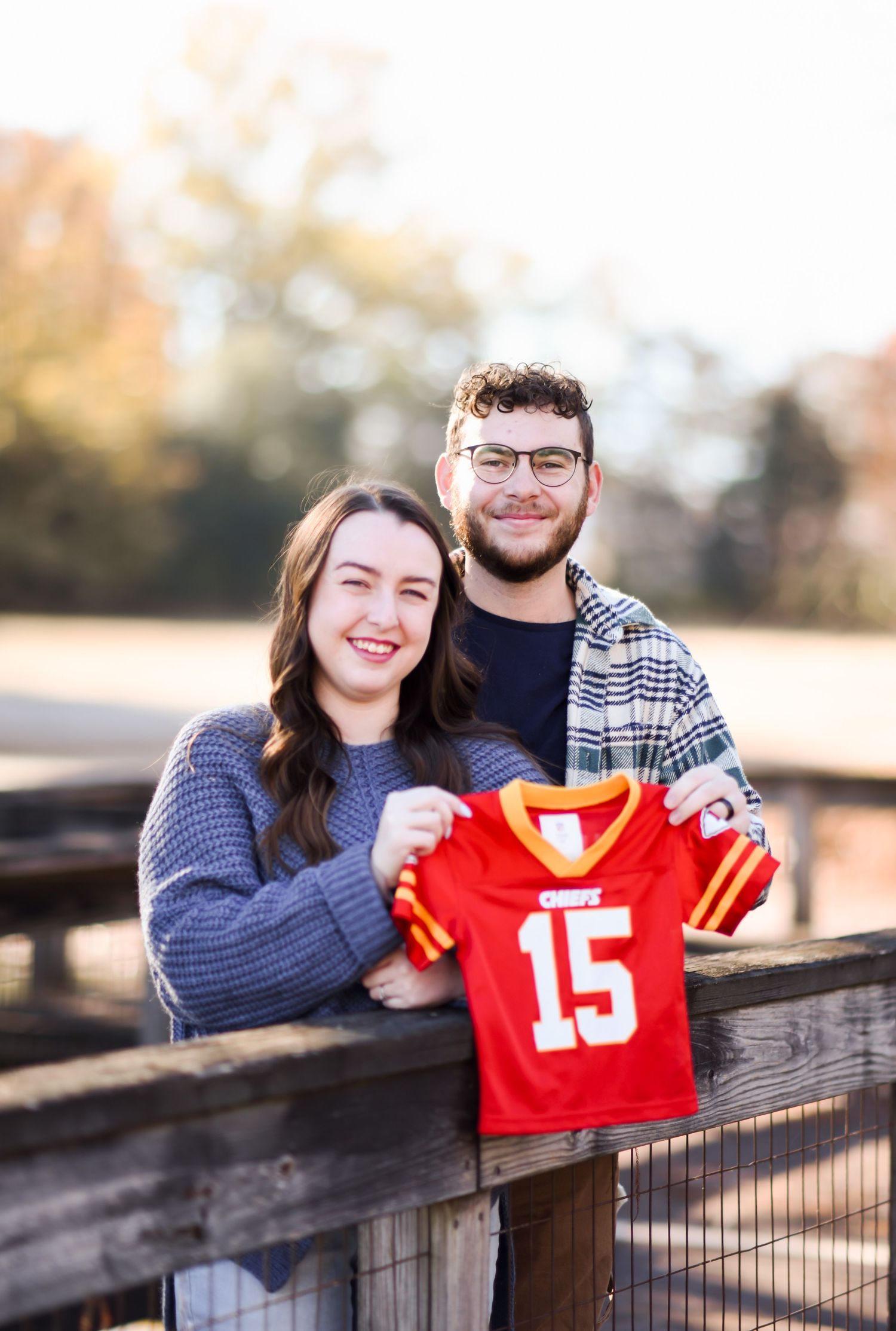 Smiling couple holding a Kansas City Chiefs jersey number 15 outdoors.