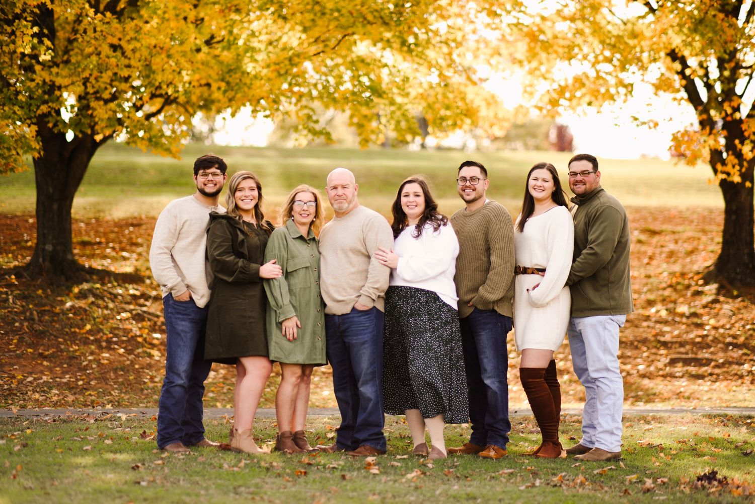 Happy family of eight posing together outdoors under colorful autumn trees.