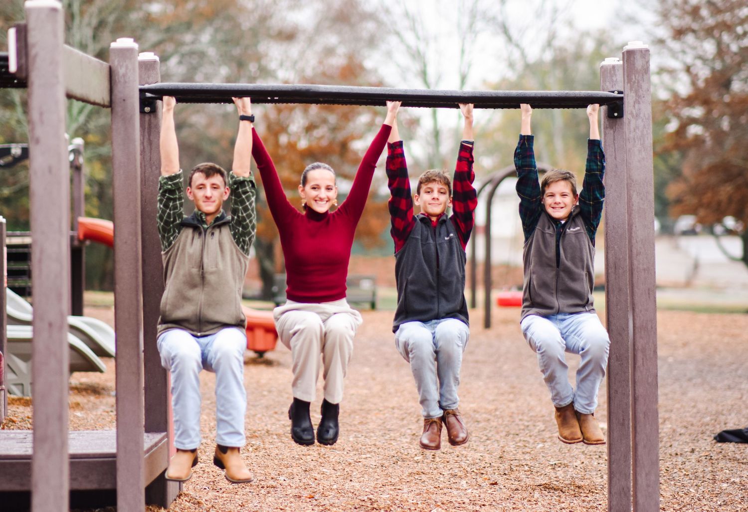Four kids hang from monkey bars at a playground during an outdoor fall family photo session.
