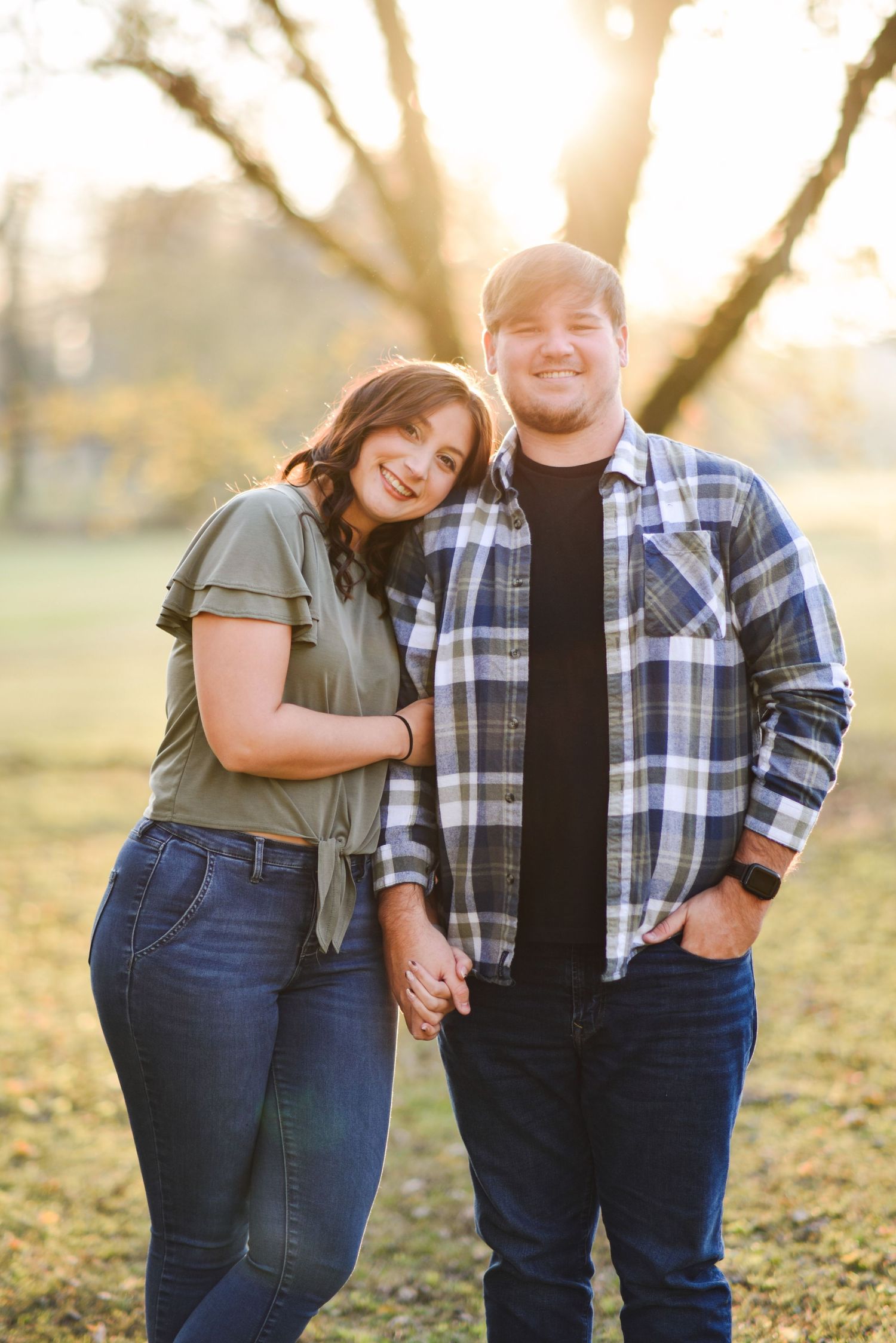 Smiling couple holding hands outdoors in warm golden hour light with trees in the background.