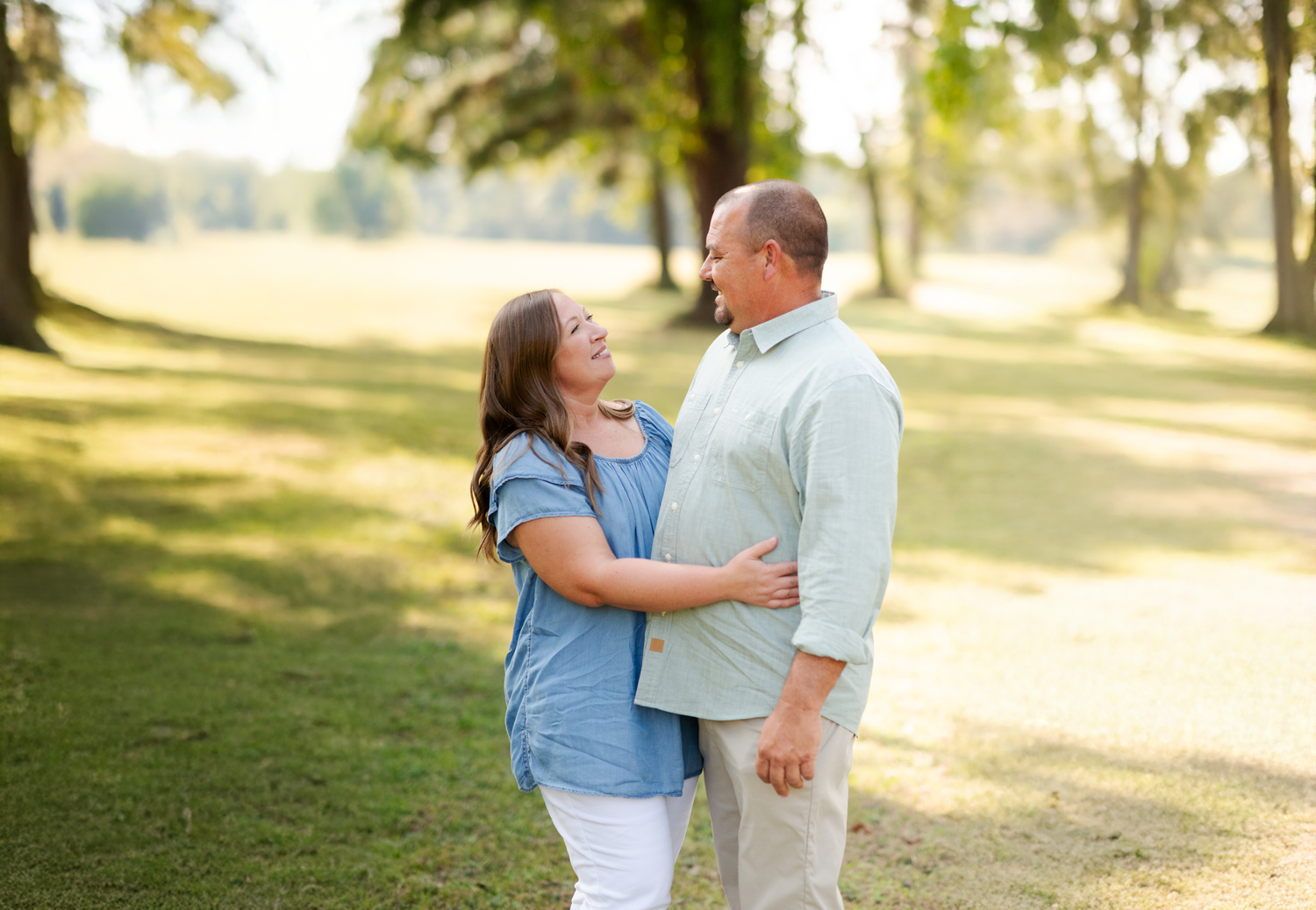 Happy middle-aged couple embracing and smiling at each other in a sunny green park.