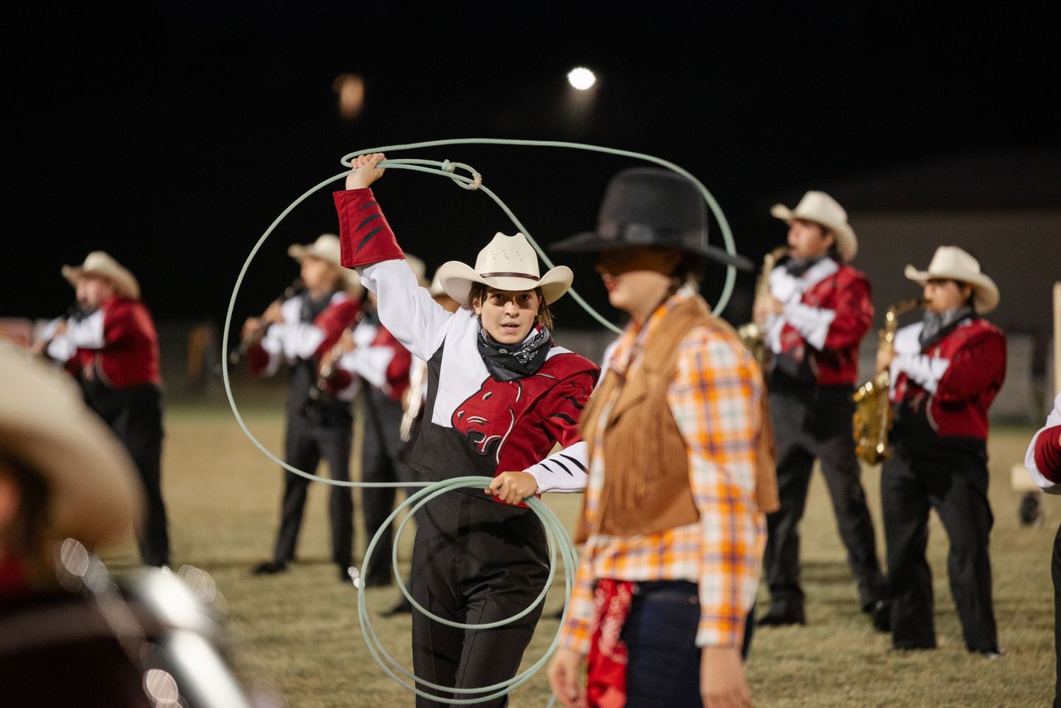Performer twirling lasso in cowboy outfit at outdoor marching band competition.