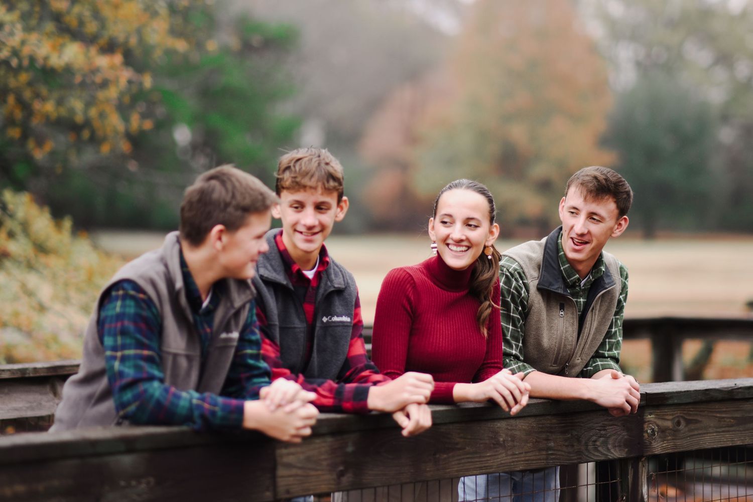 Four happy teenagers leaning on a wooden fence laughing outdoors in fall.