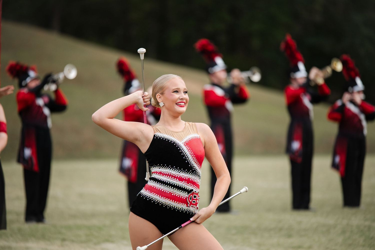 Smiling baton twirler in red and black costume performing with marching band.