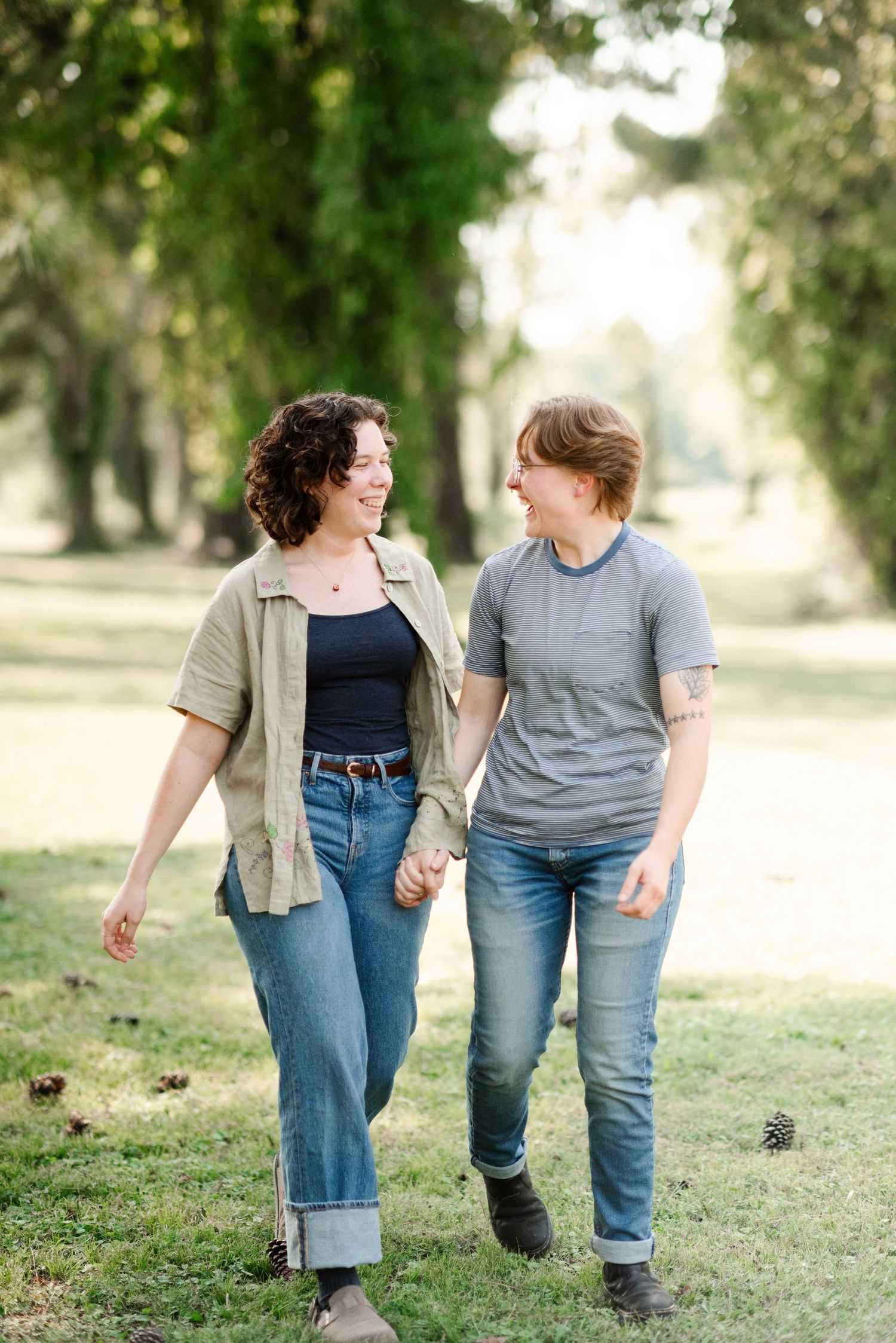 Two women holding hands and smiling at each other while walking in a sunny park.