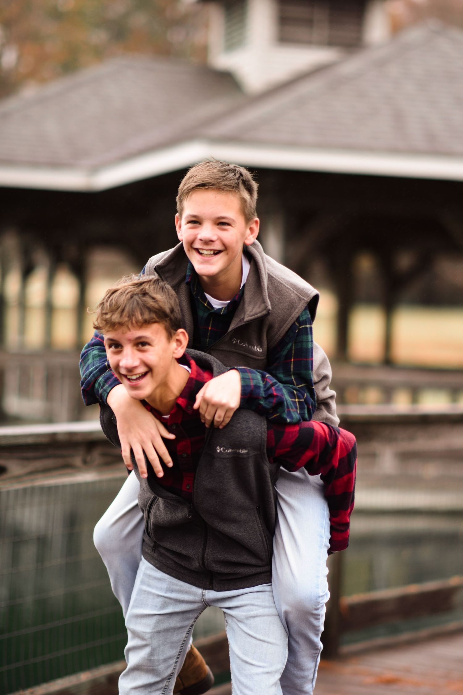 Two boys laughing as one gives the other a piggyback ride outdoors.