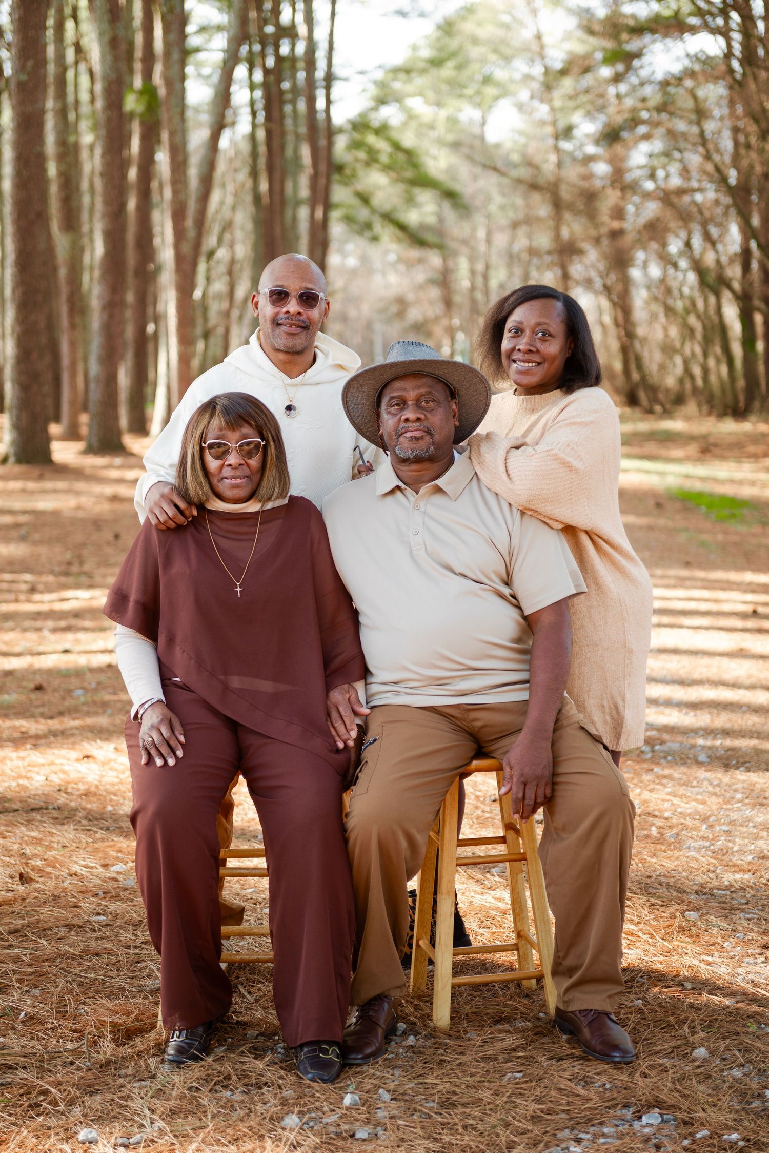 Family of four poses together in pine forest, two seated and two standing behind them.