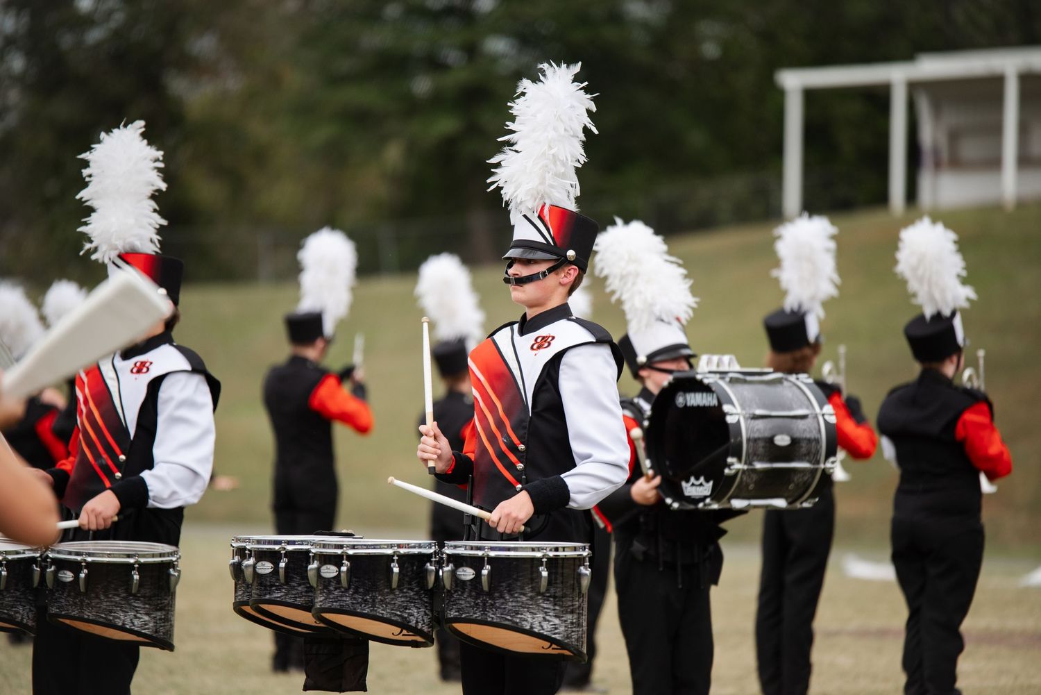 Marching band drummers in red and black uniforms playing snare drums on a green field.