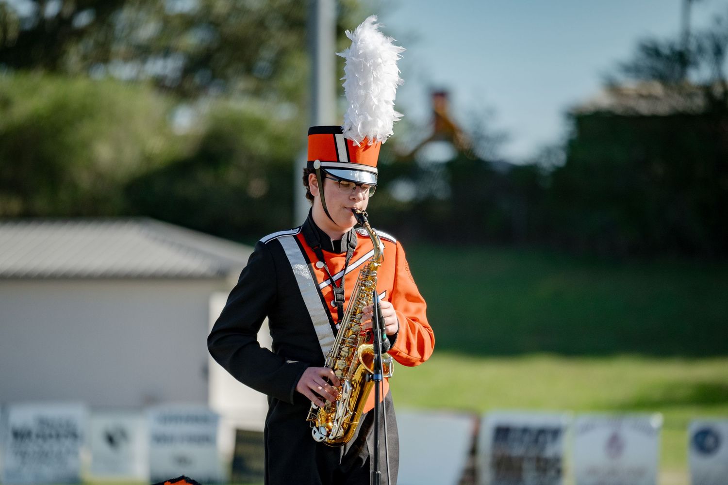 A marching band saxophonist in an orange and black uniform performs during an outdoor competition.