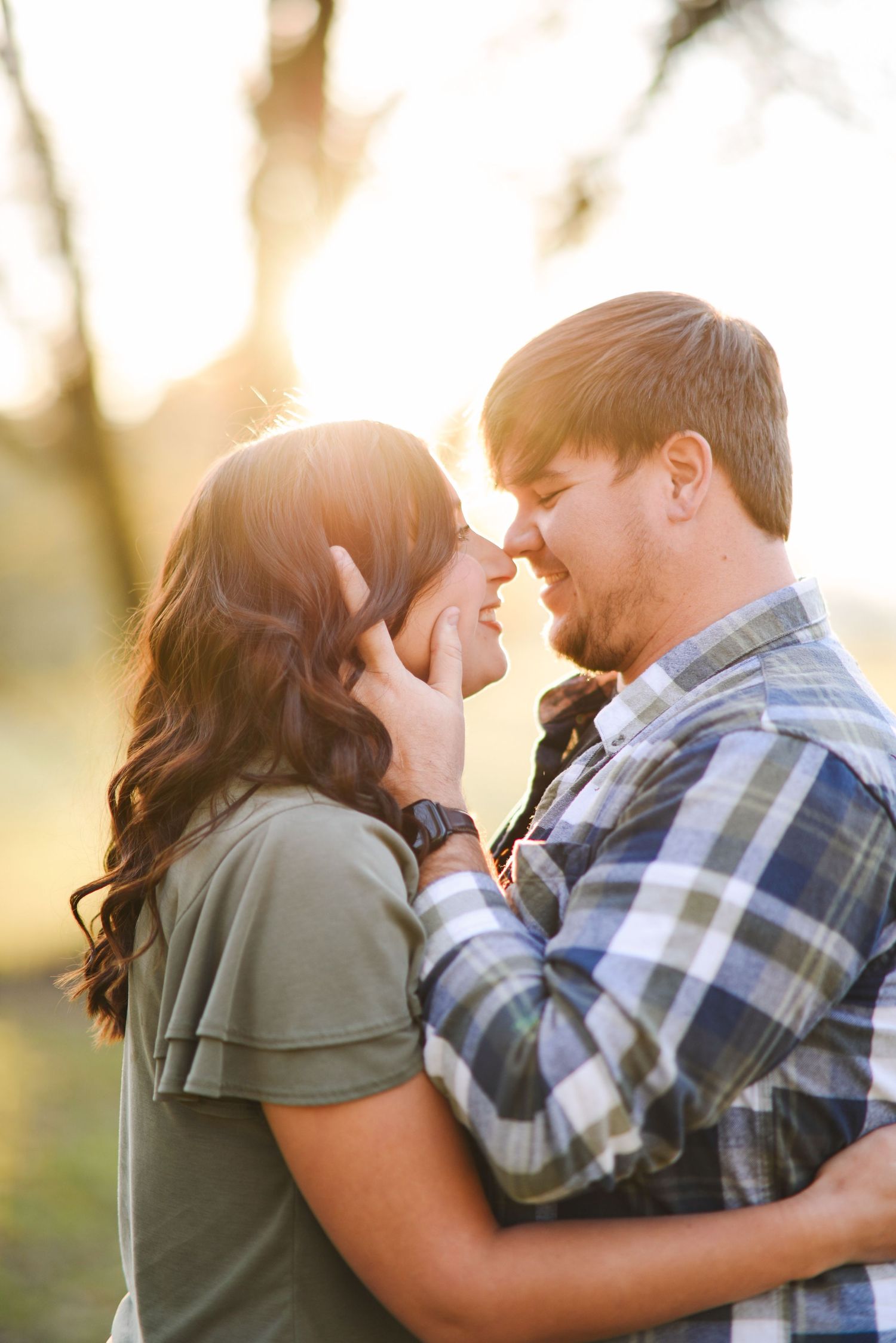 Romantic couple nearly kissing in glowing sunset light, embracing closely outdoors in a park.