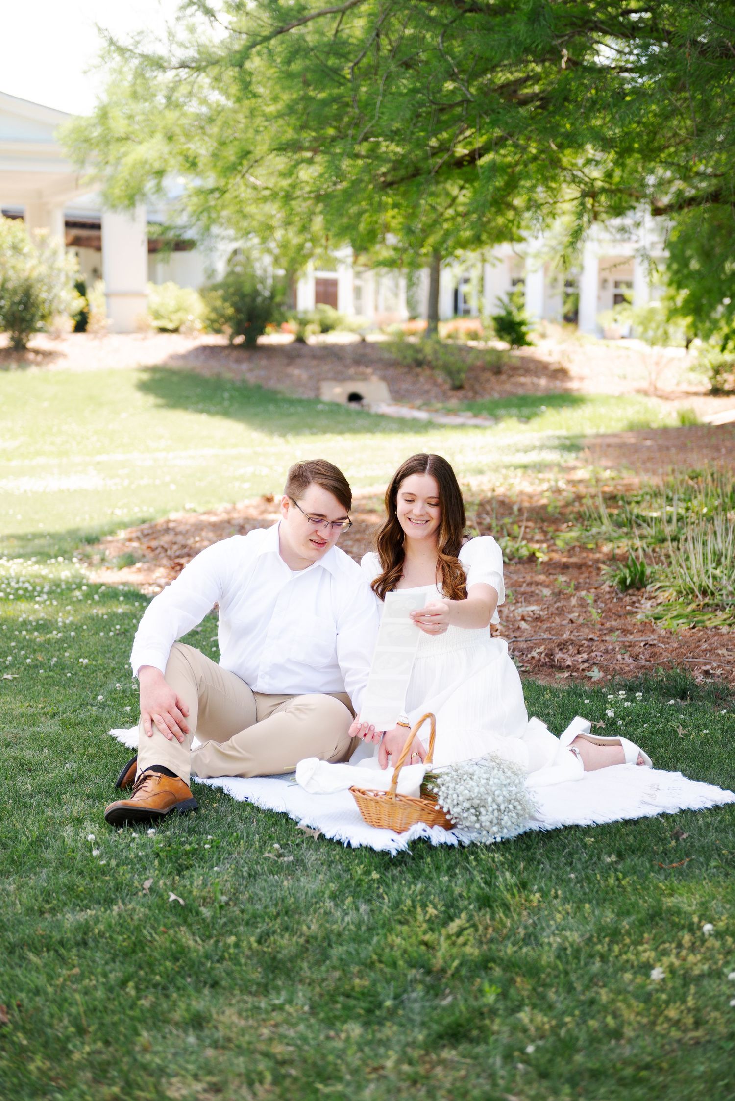 A couple sits together on a white blanket in a garden, sharing a joyful picnic moment.