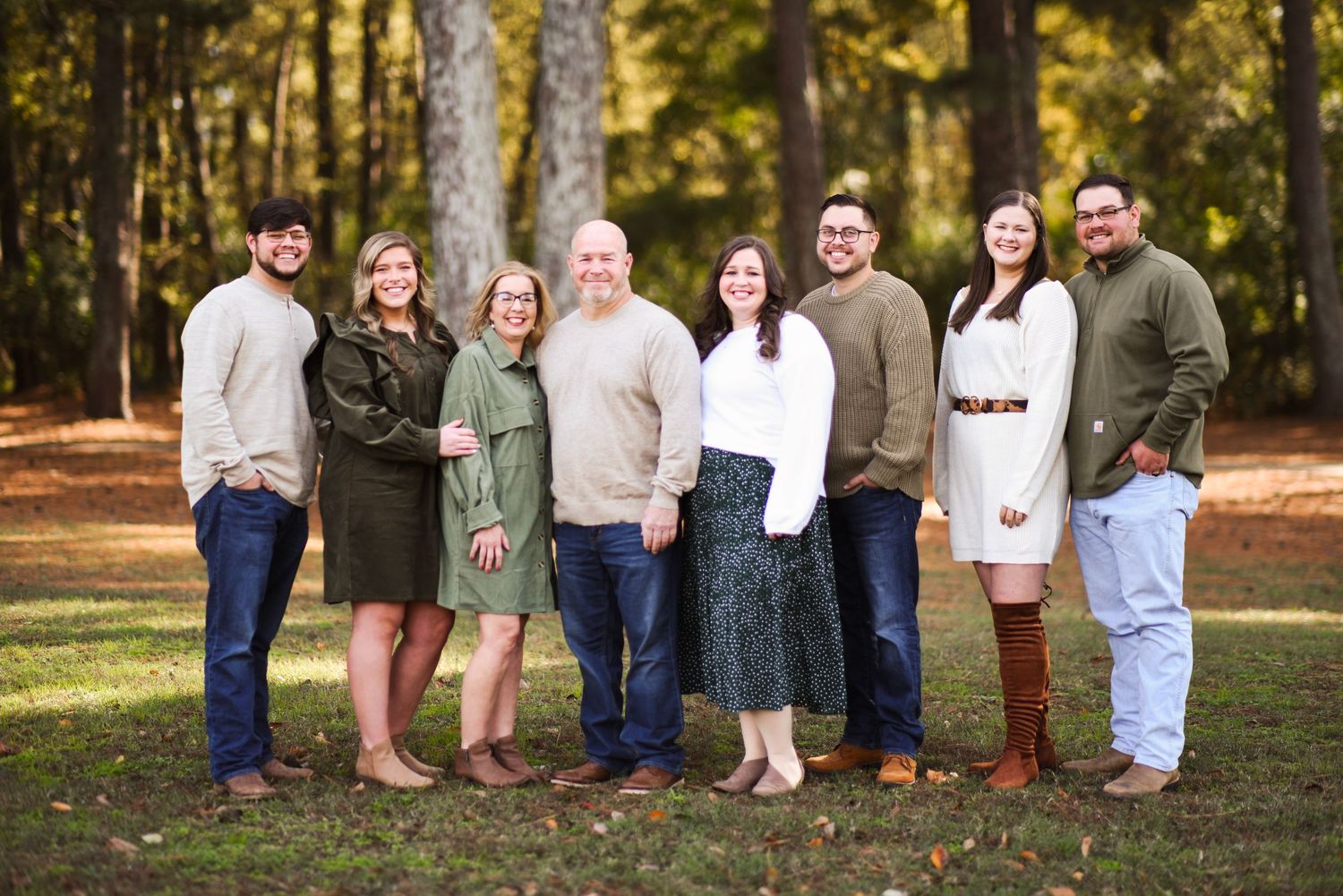 Family of eight posing together in a pine forest during fall.