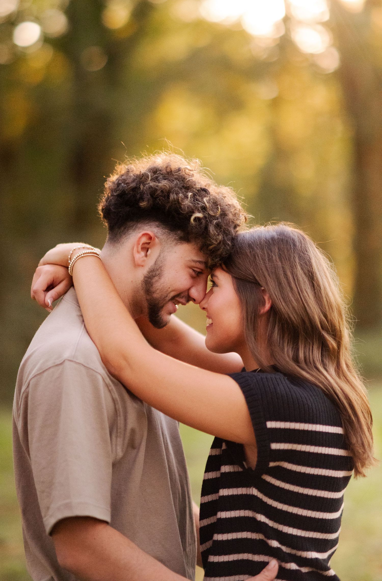 Happy couple embracing and touching foreheads in a romantic outdoor park setting at sunset.