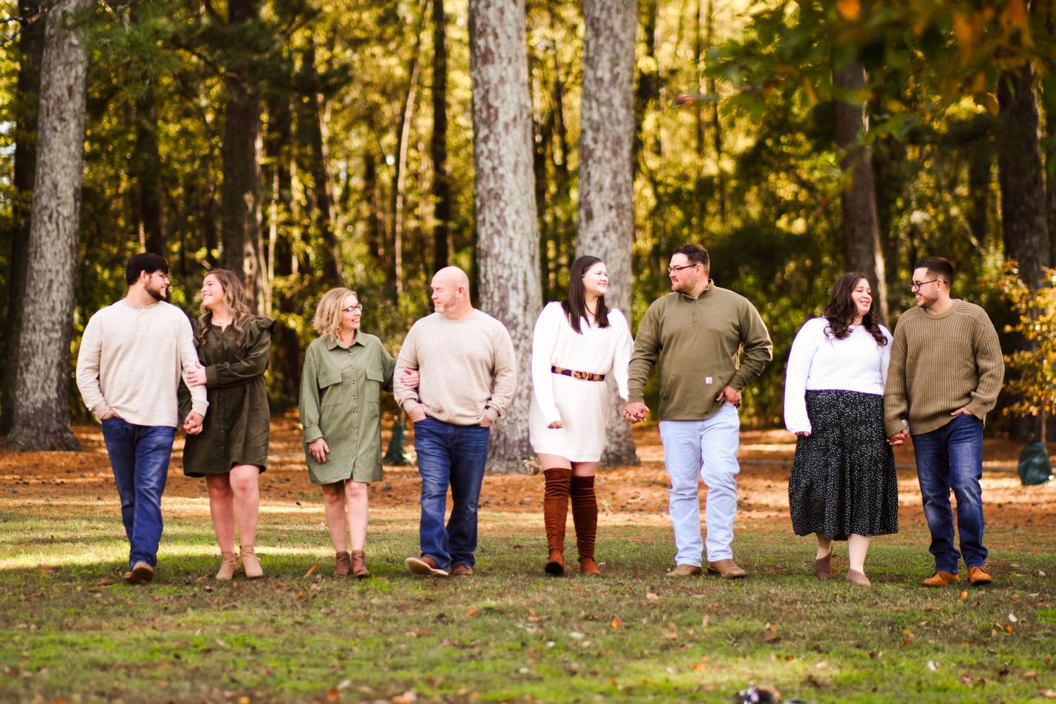 Family of eight walks together laughing through a wooded park with fall foliage background.