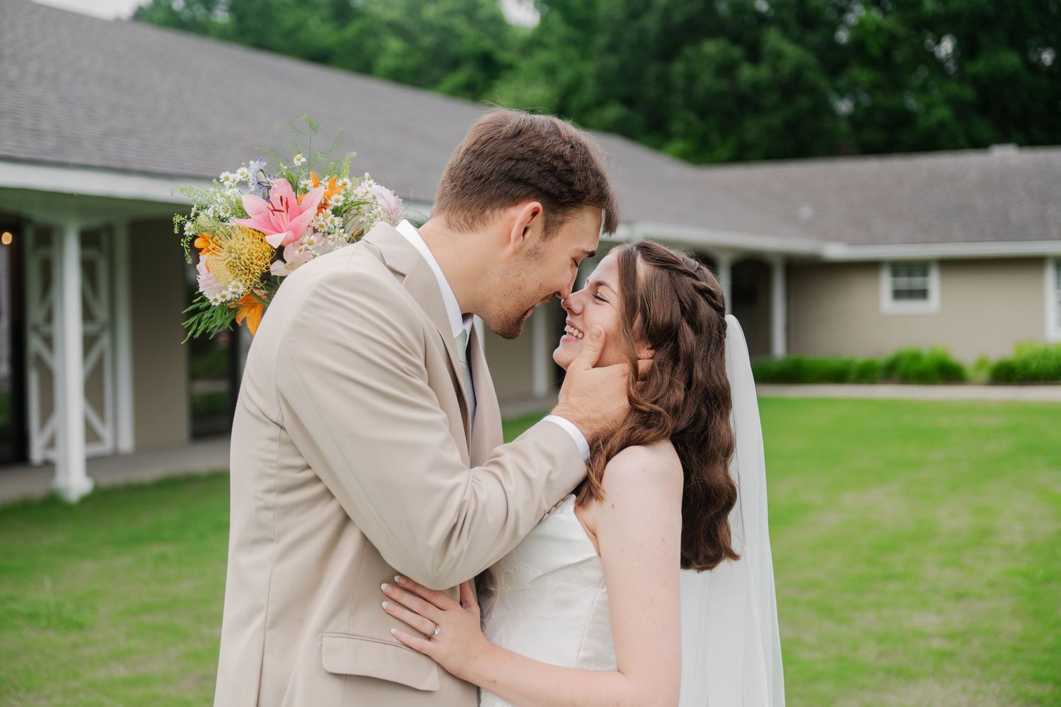 Bride and groom sharing a romantic moment outdoors, nearly kissing in front of white venue.