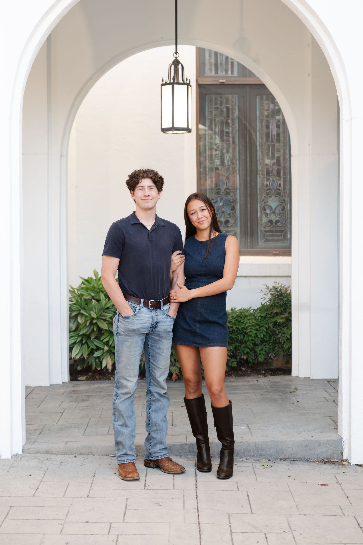 Young couple in matching navy outfits posing under a white arch with an ornate door backdrop.