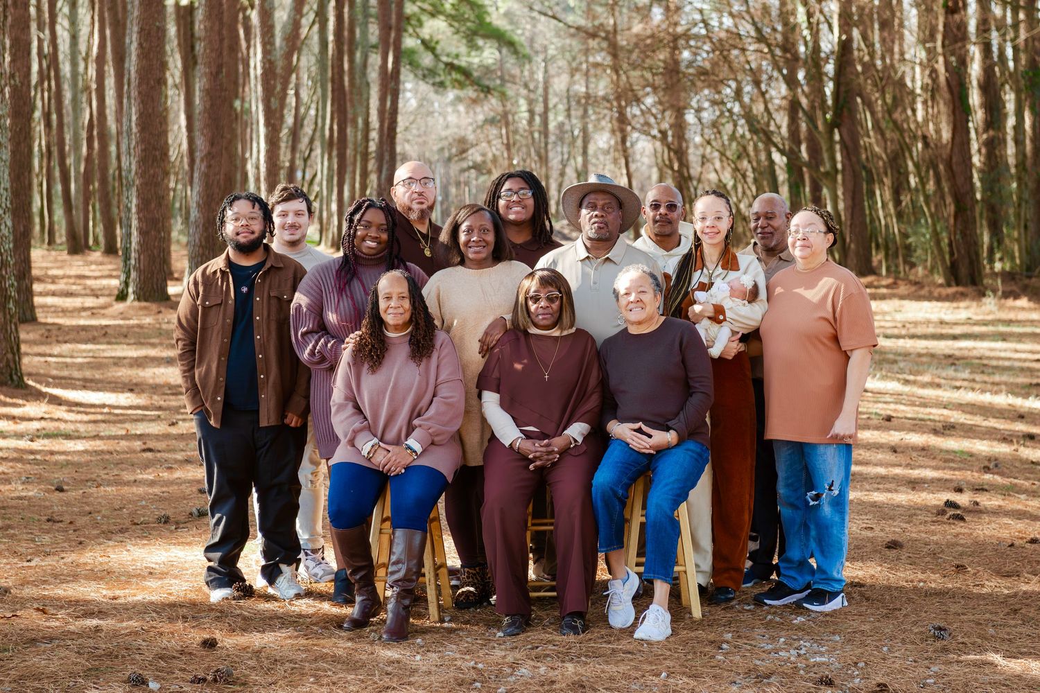 Large multigenerational family group portrait taken outdoors in pine forest with autumn foliage.