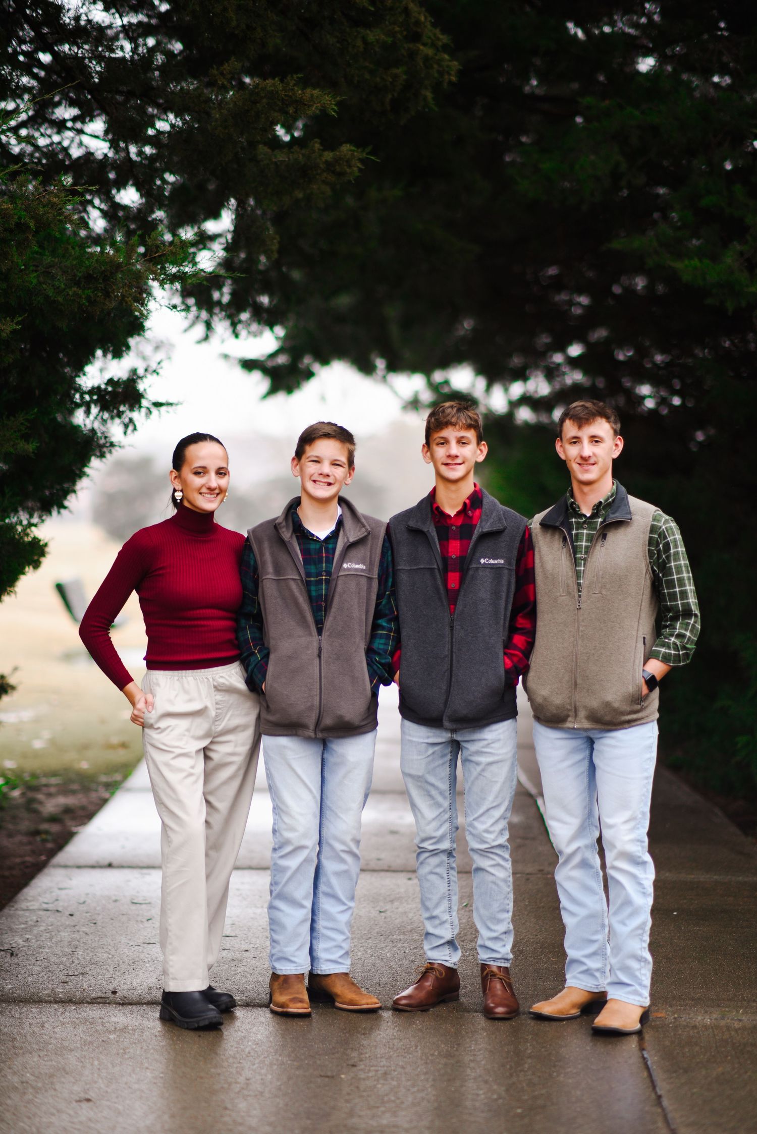Four teenagers posing together outdoors wearing vests and plaid shirts.
