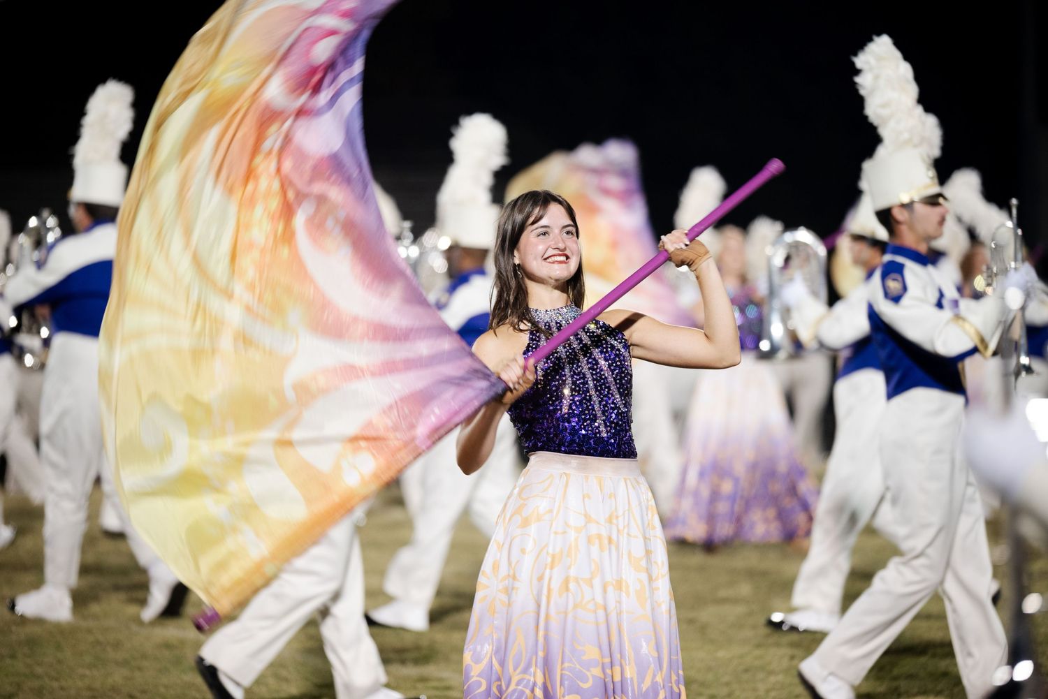 Color guard performer twirling colorful silk flag during marching band night performance.
