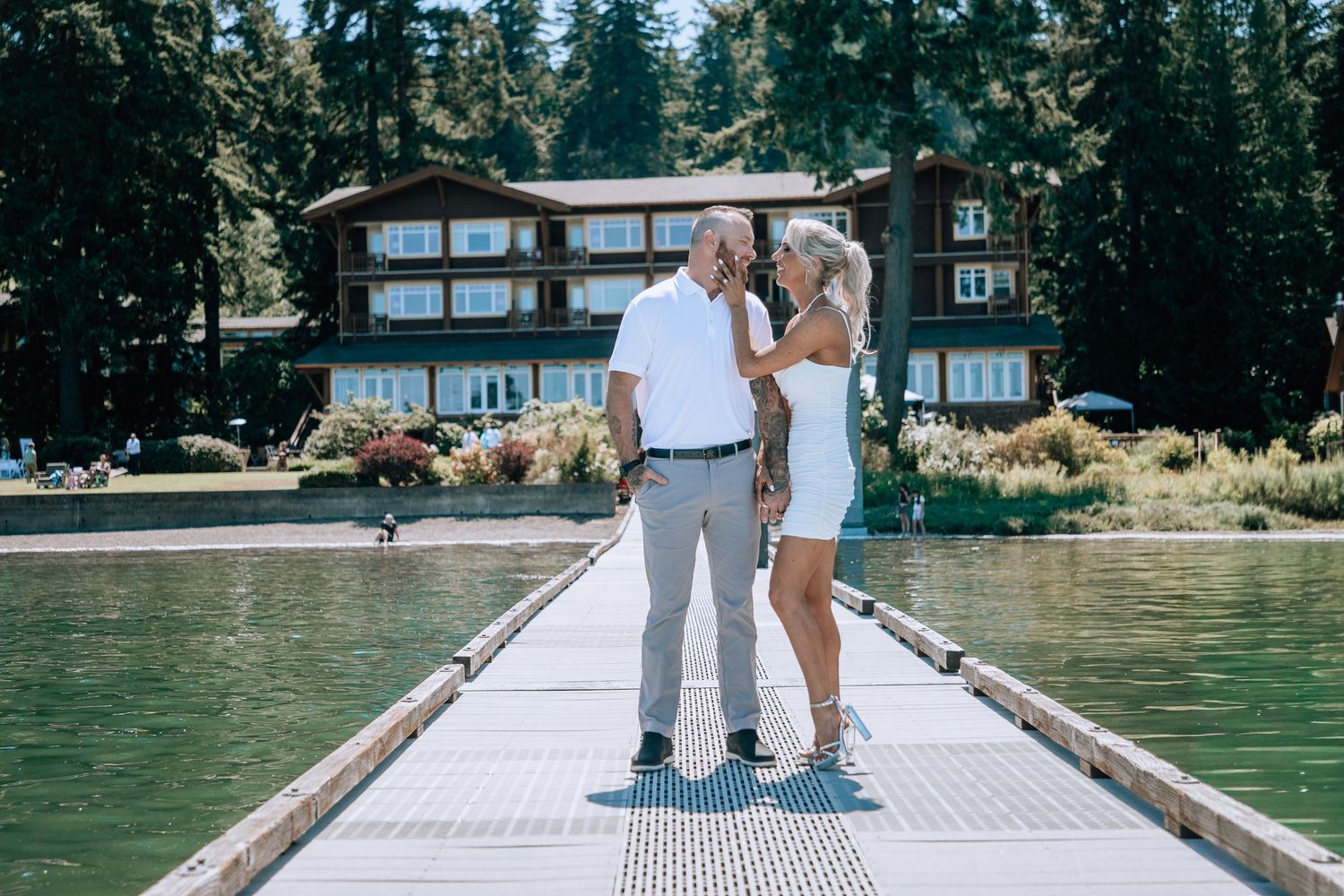 Couple shares a tender moment on a lakeside dock with a mountain lodge behind them.