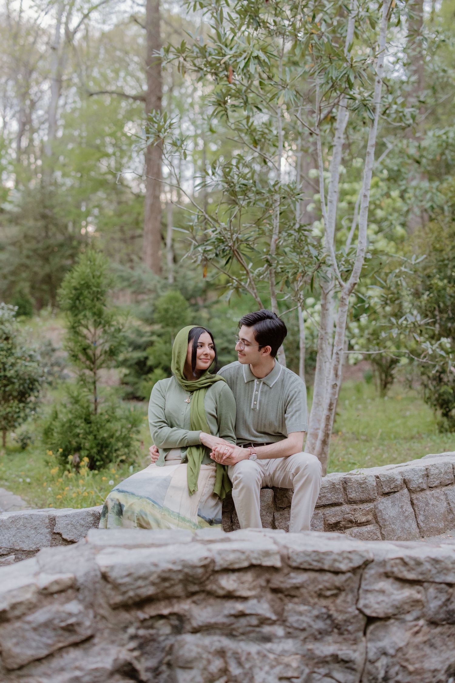 A couple sits together on stone steps surrounded by trees and greenery in a peaceful outdoor setting.
