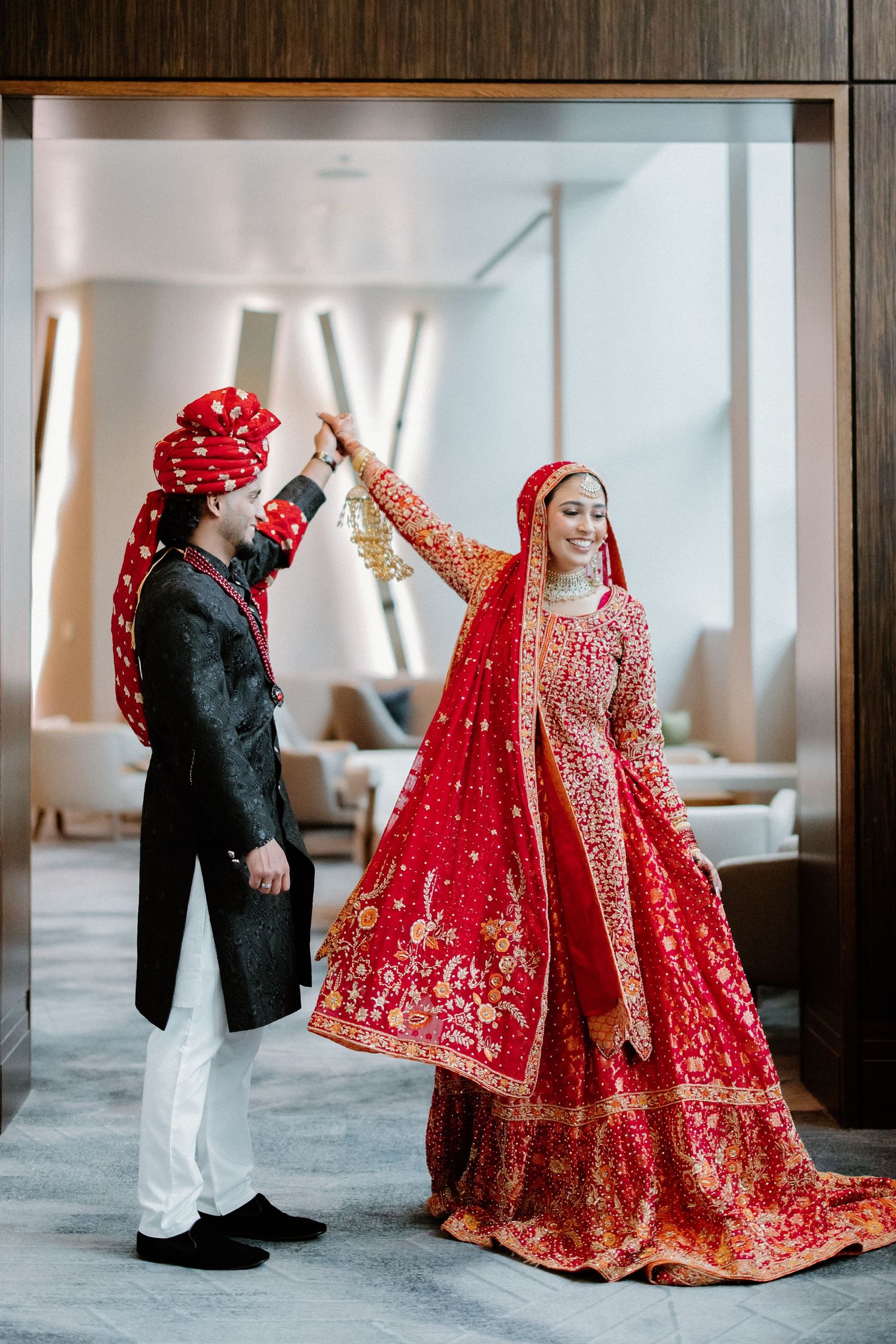 Rich red and gold traditional South Asian bridal lehenga shown in multiple poses against a minimalist interior setting.
