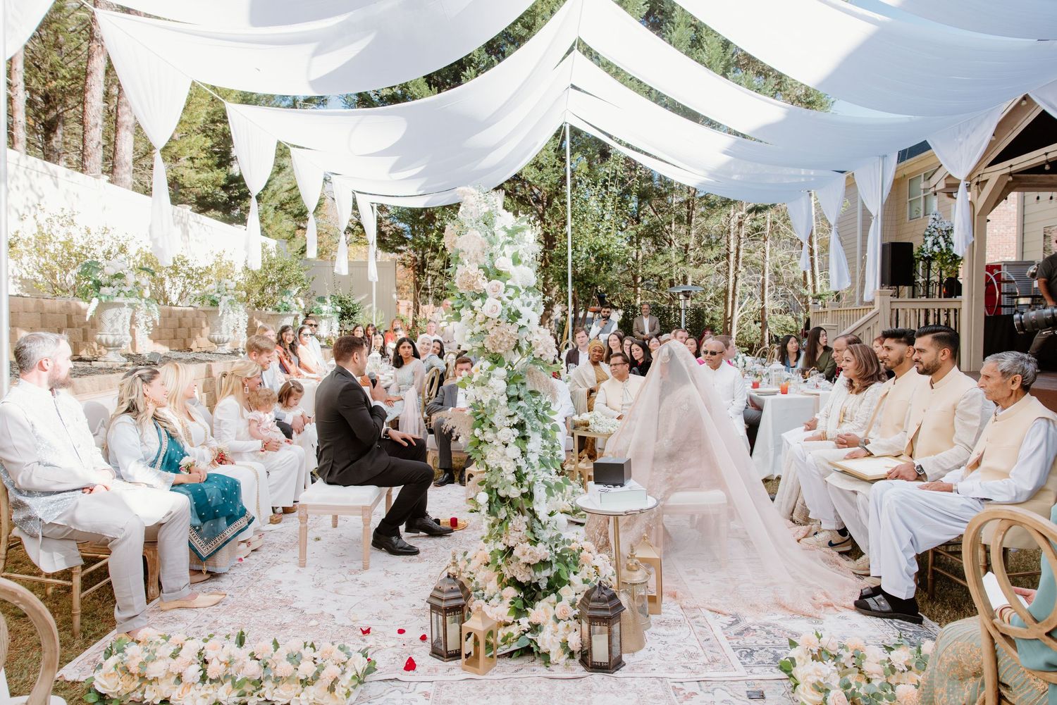 An elegant outdoor wedding ceremony under white fabric draping with lush greenery and floral arrangements.