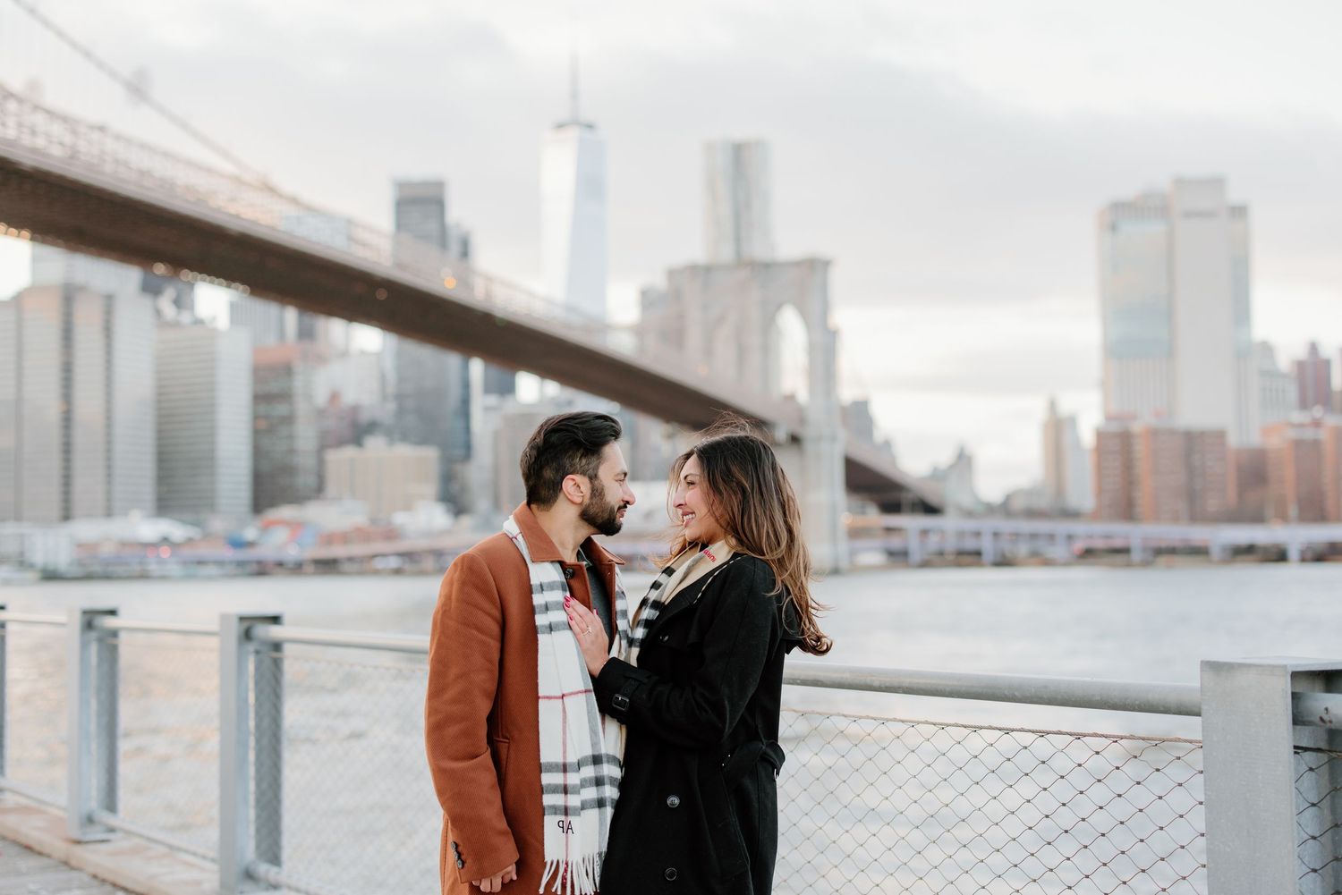 Two figures share an intimate moment while embracing on a rooftop with a hazy city skyline in the background.