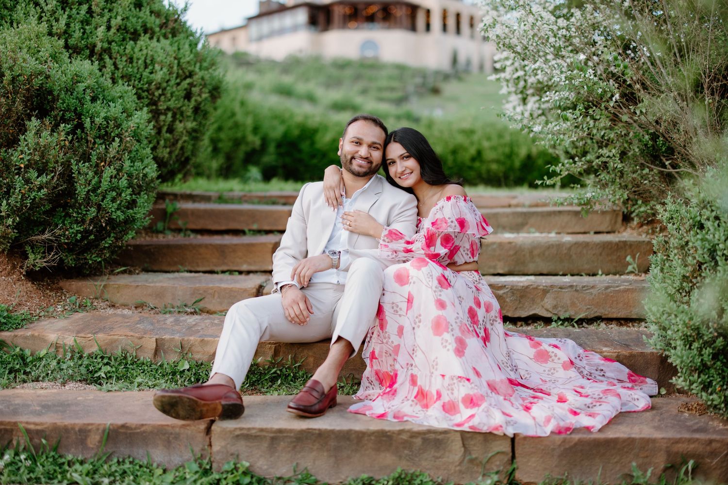 Couple sitting on stone steps outdoors with woman wearing floral pink dress and man in white outfit.