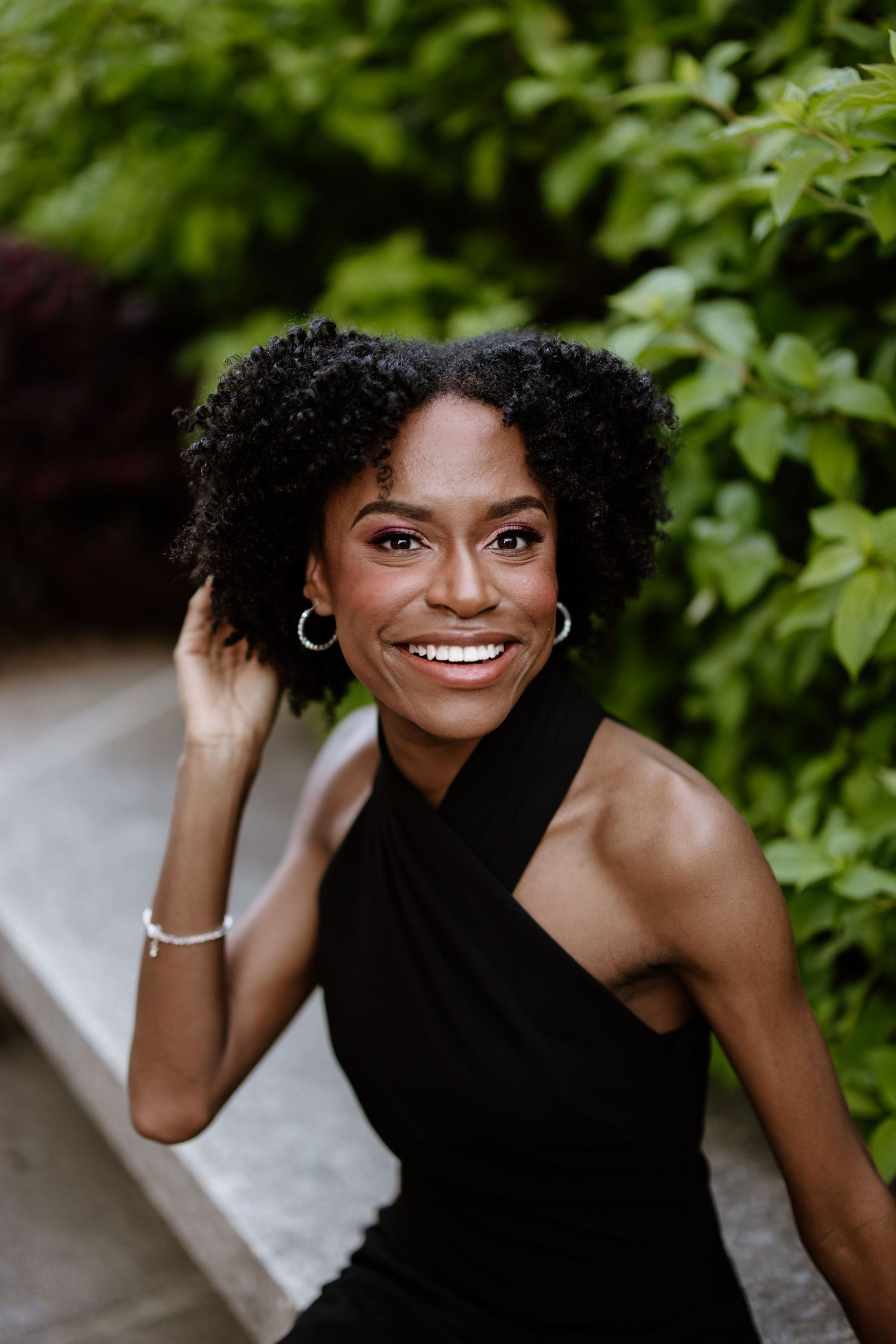 A person in a black dress poses playfully against a leafy green background in a photo sequence.