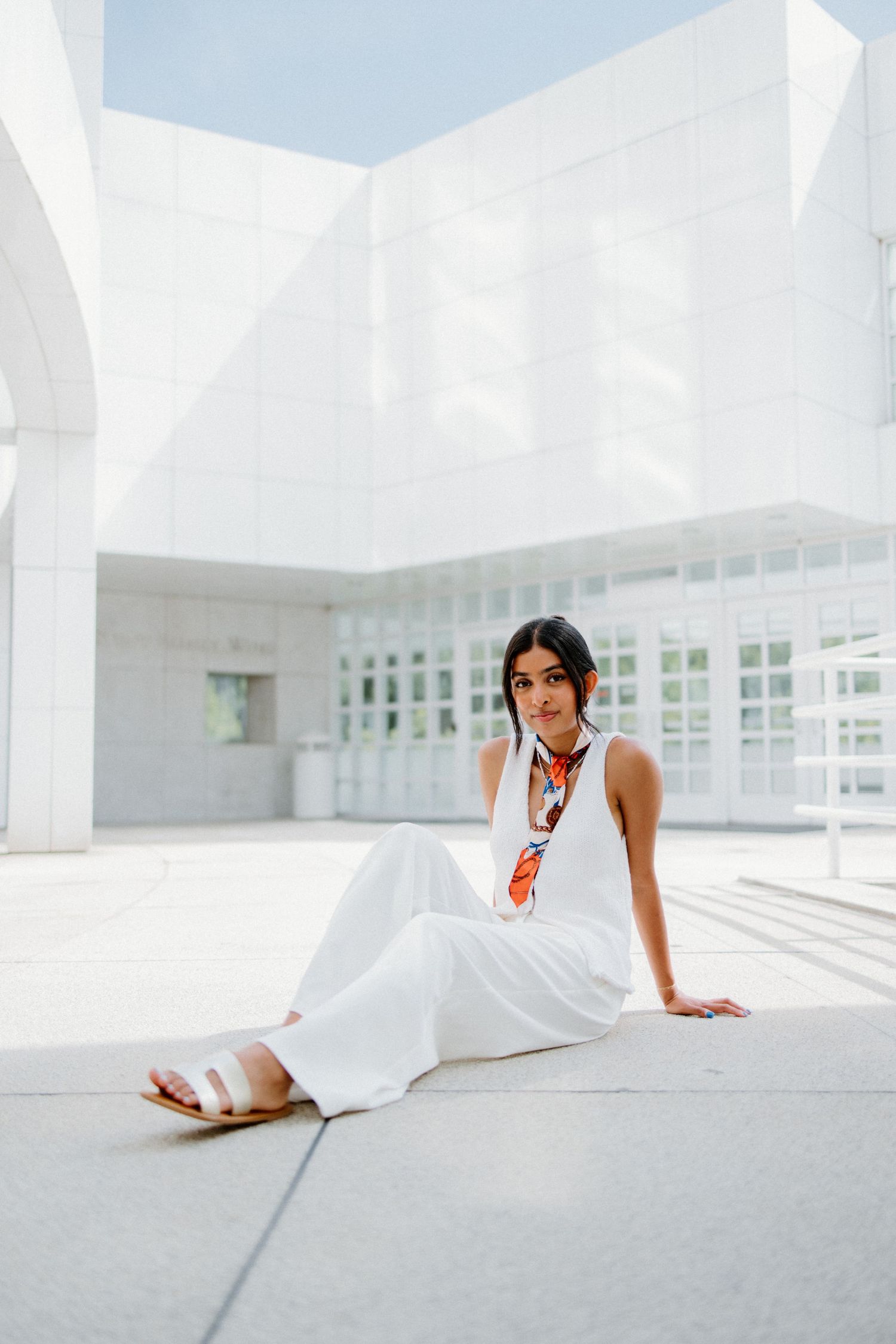 Person in white outfit elegantly posed on light concrete floor with modern minimalist architecture surrounding them.