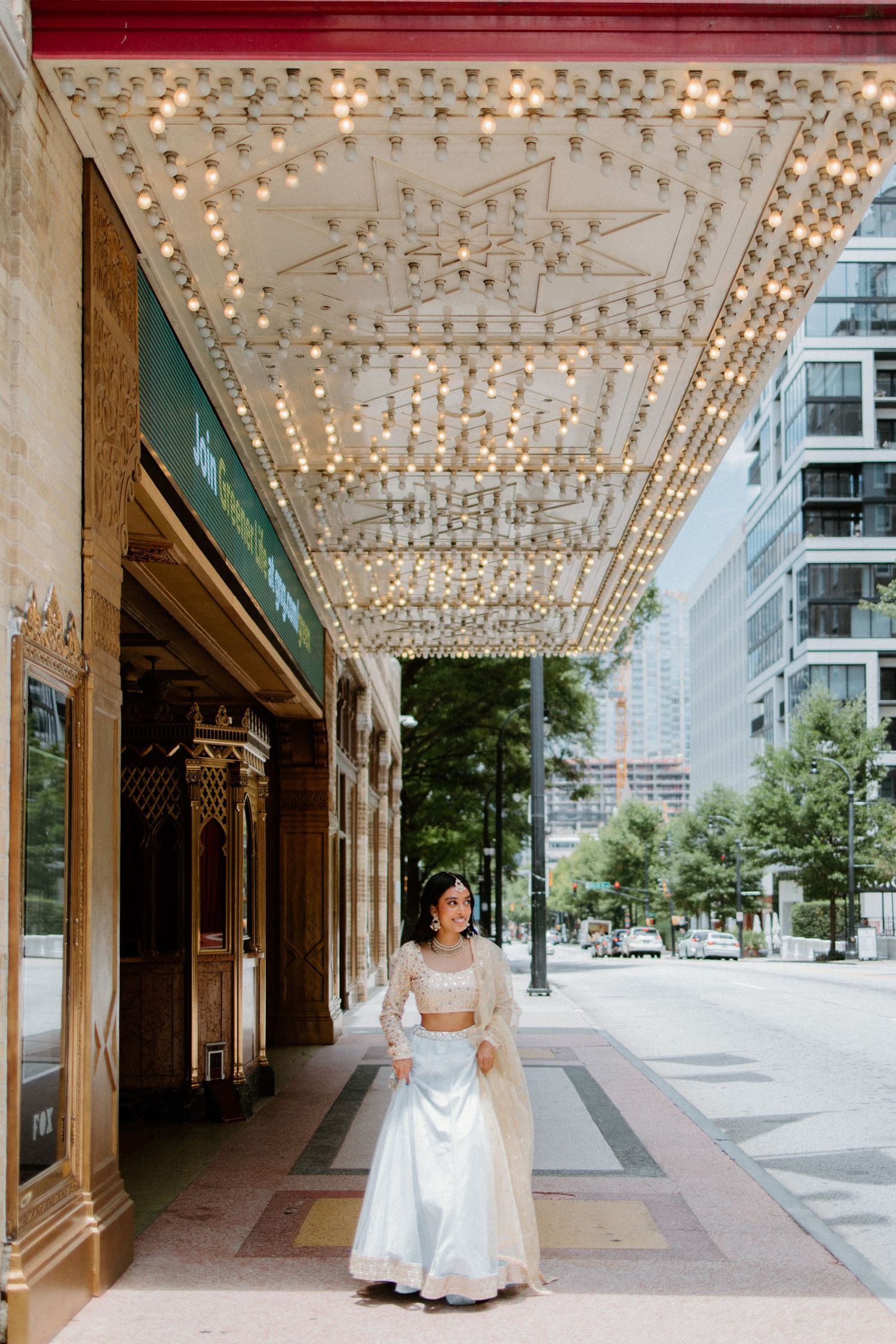 Ornate marquee with sparkling lights decorates the entrance of an urban building along a quiet city sidewalk.