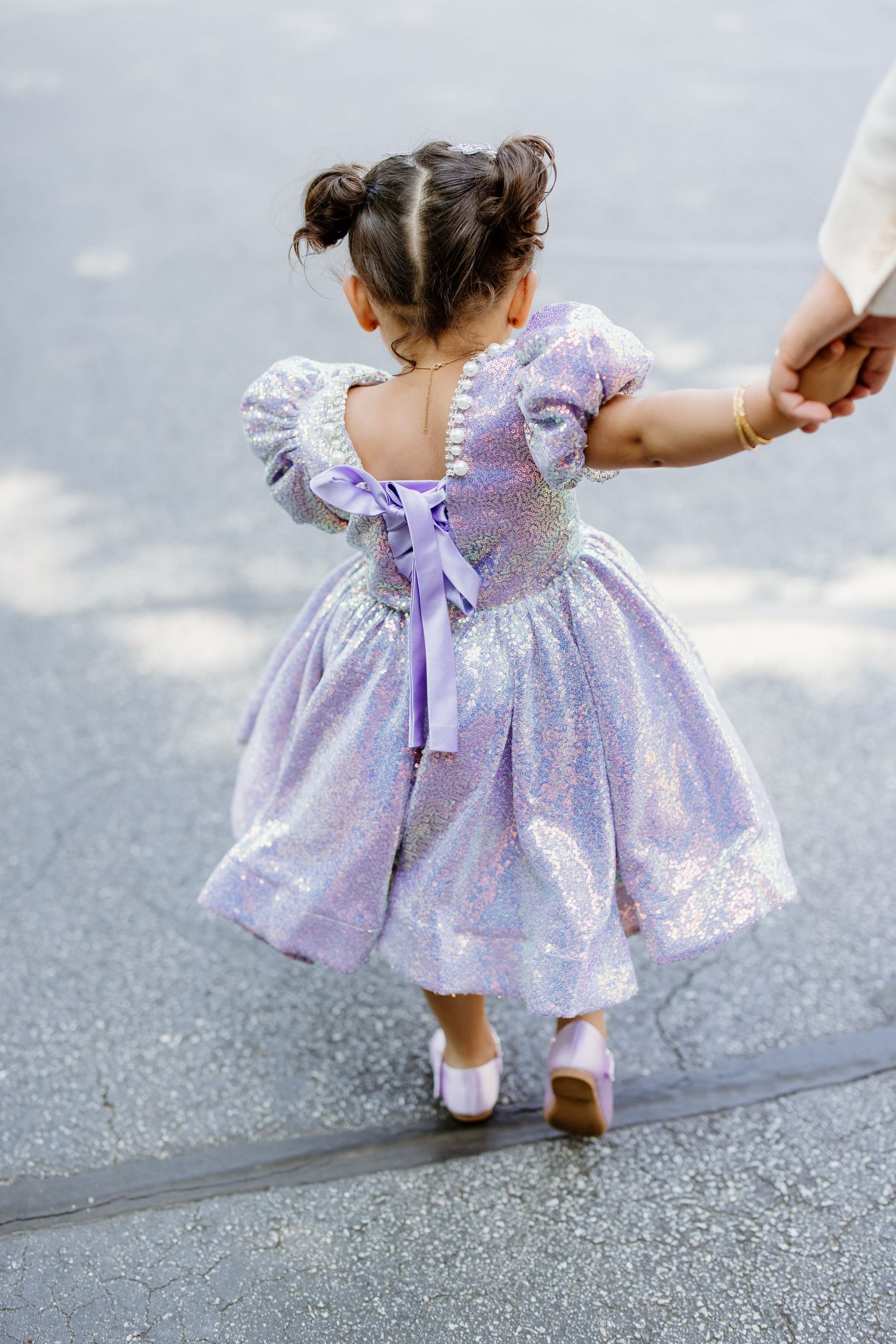 A figure in a lavender sparkly dress twirls around playfully on pavement showing off the dress's flowing skirt and bow details.