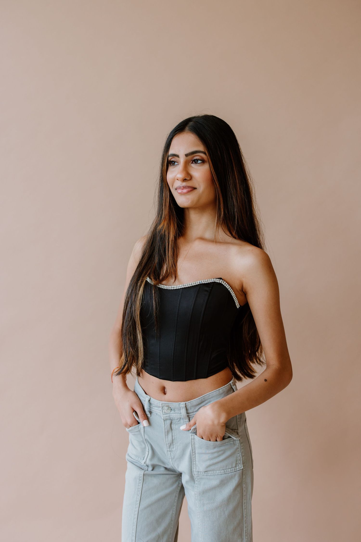 A fashion photoshoot series features a model in a black crop top and high-waisted light wash jeans against a beige wall.