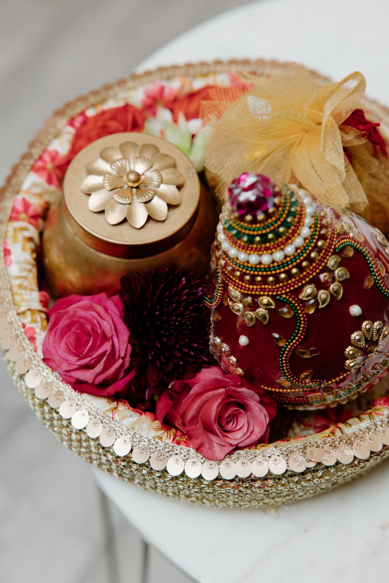 Beautiful Indian wedding decor with decorated red ornament, pink roses, and golden container on an ornate beaded thali plate.