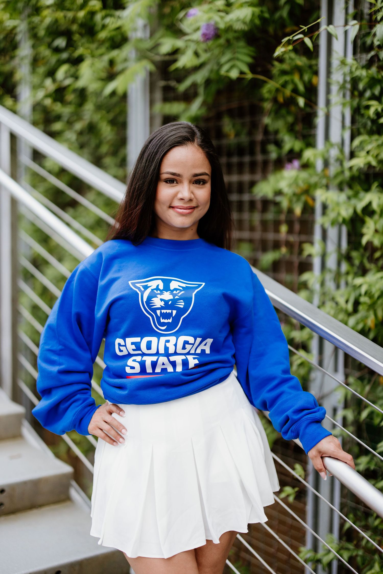 Student wearing a bright blue Georgia State University sweatshirt and white pleated skirt poses on outdoor steps.